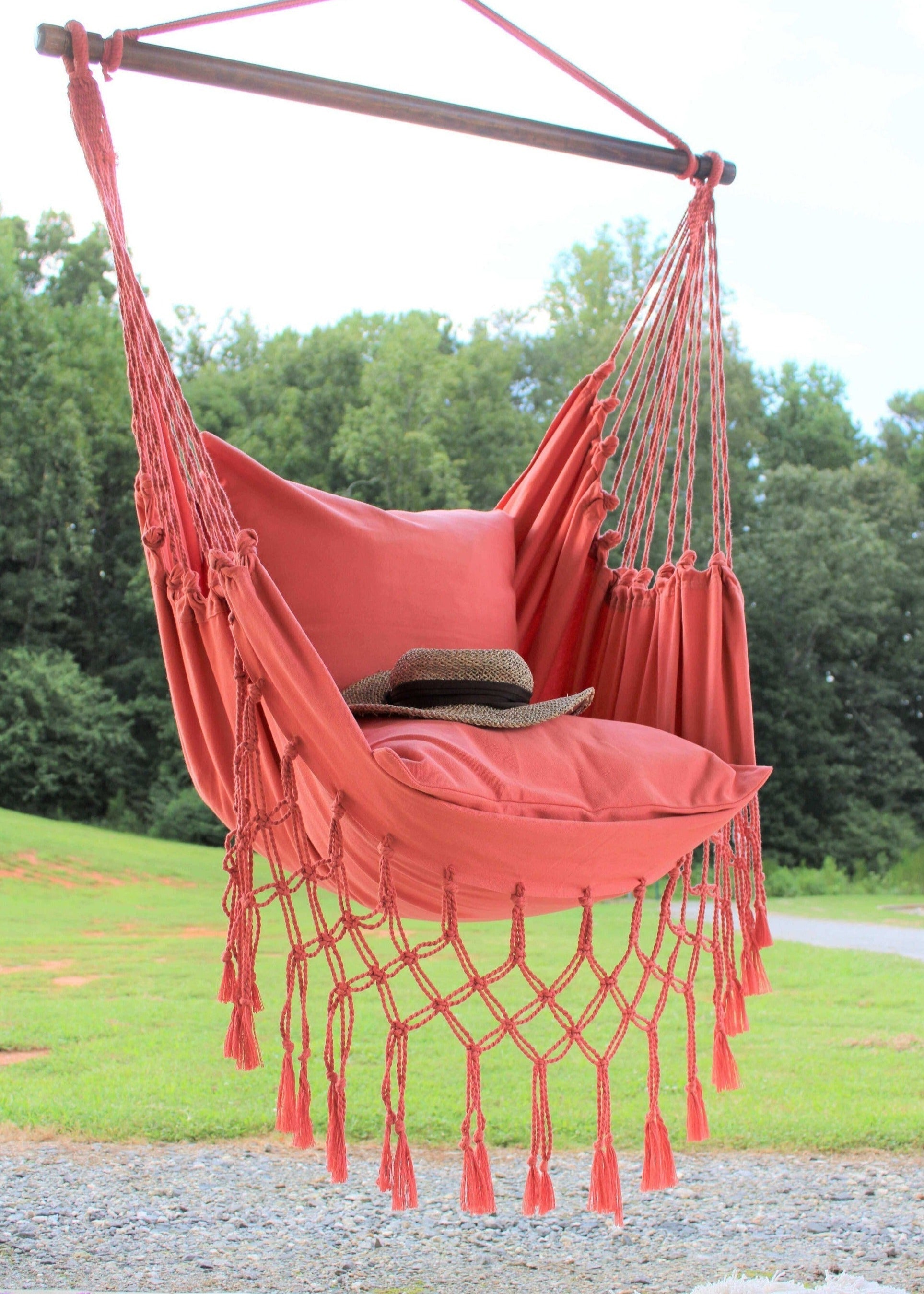 Red hammock chair with tassels hanging outdoors on a sunny day.