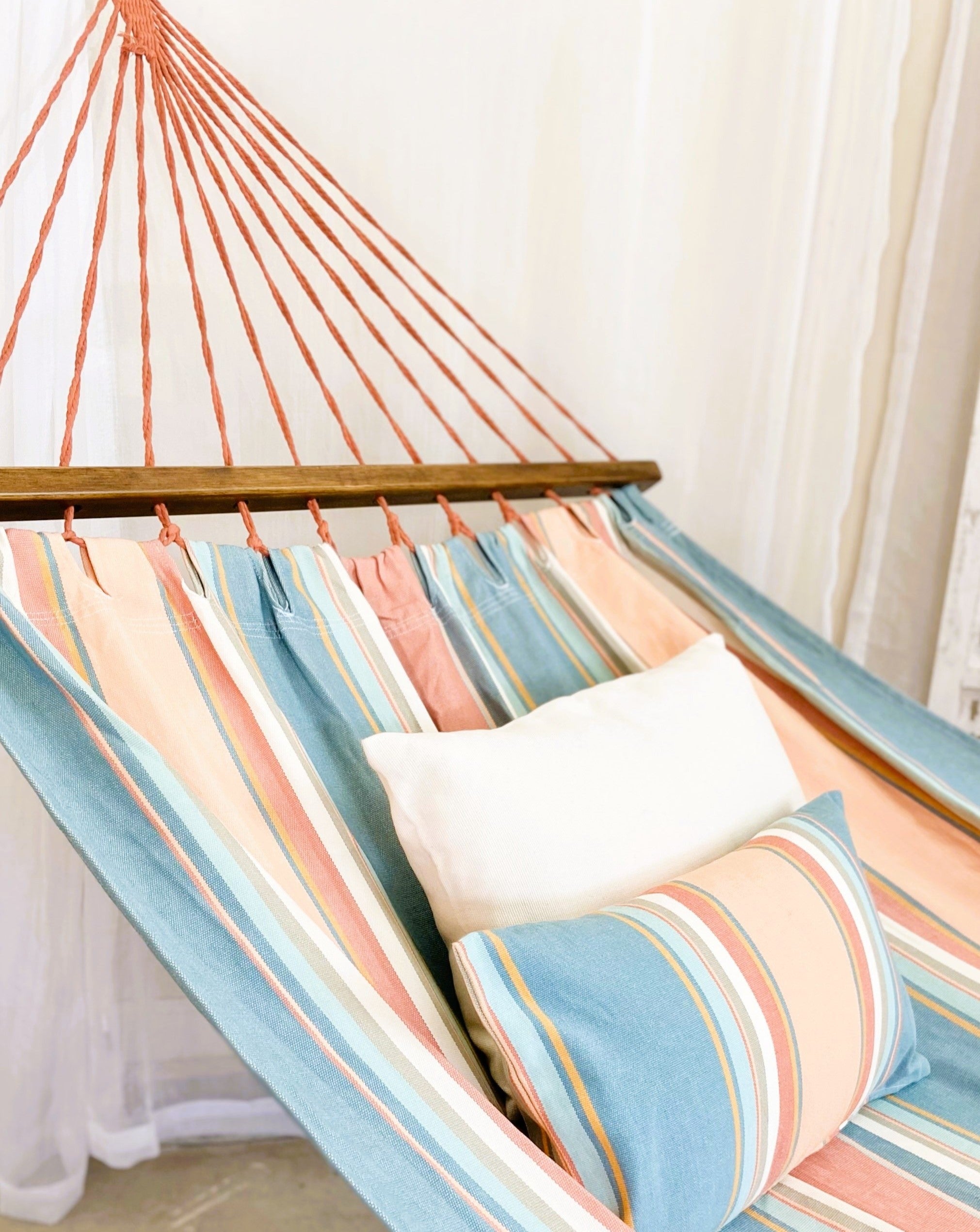 Striped hammock with a pillow against a white curtain background
