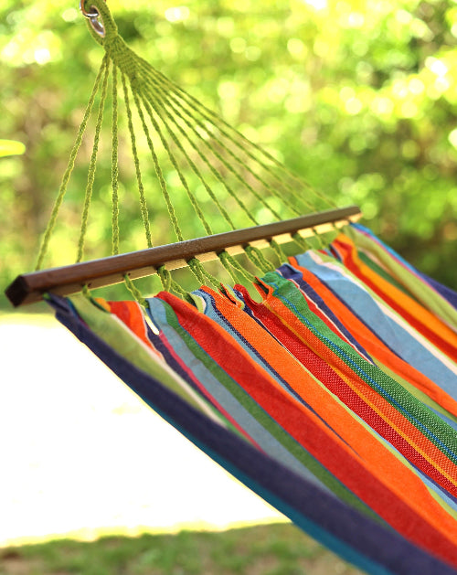 Colorful striped hammock hanging outdoors with a blurred green background