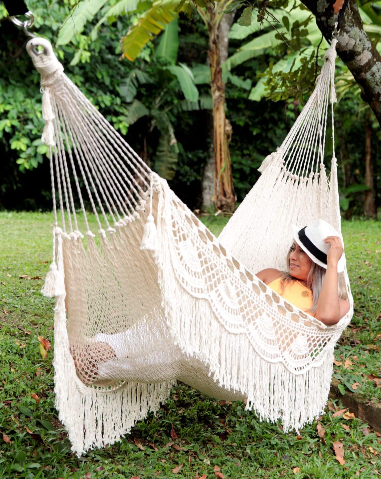 Person relaxing in a white hammock with fringe in a garden setting