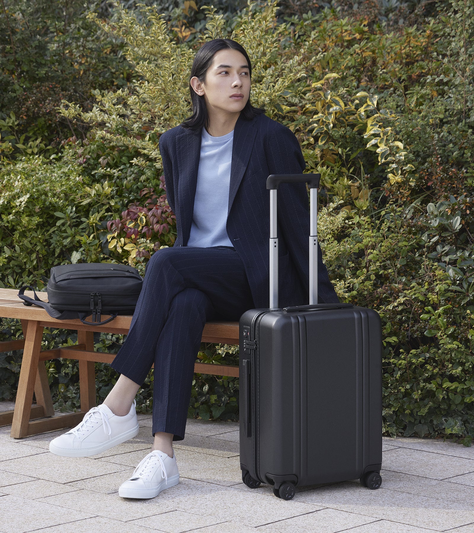 Person sitting with a black suitcase outdoors