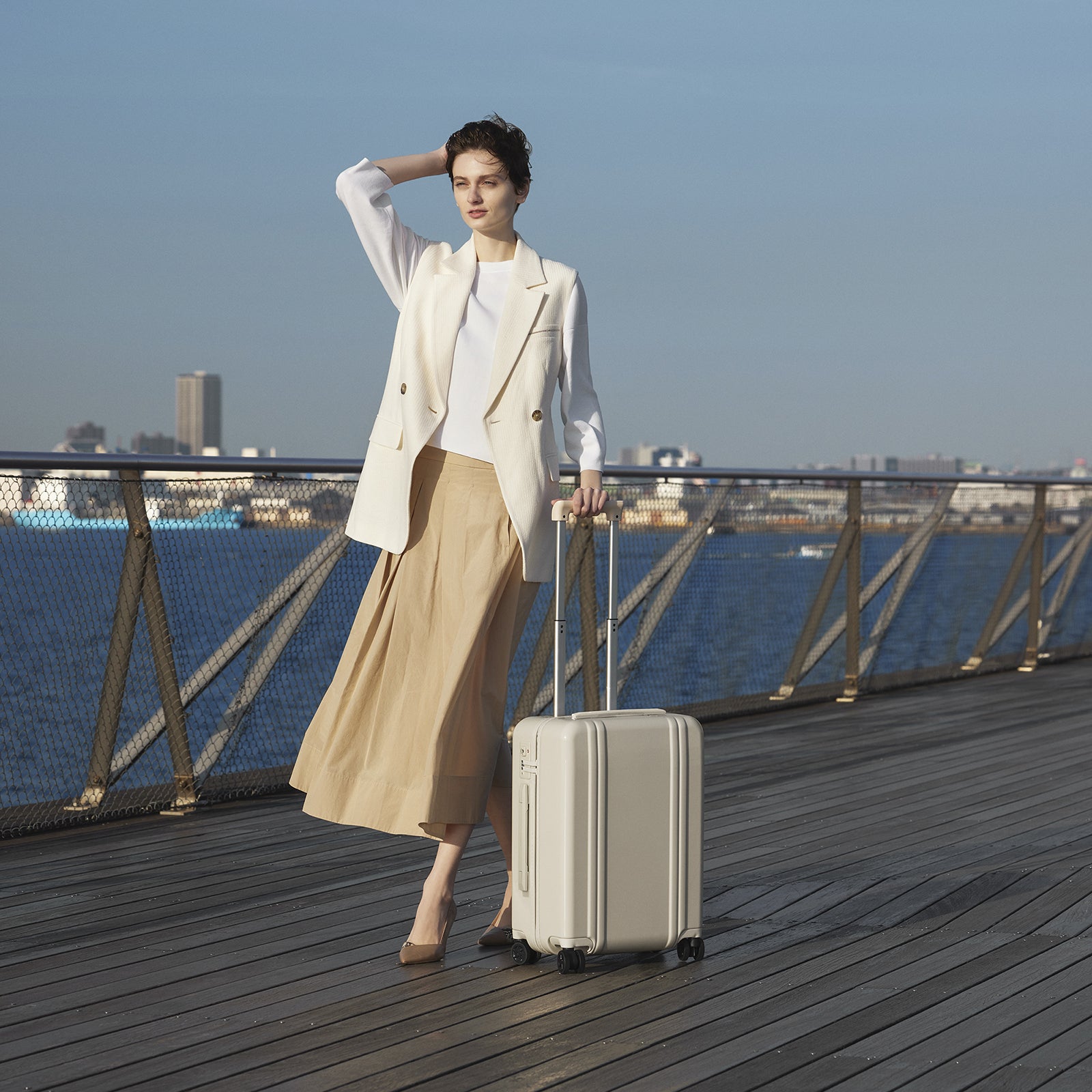 Woman with a beige suitcase on a wooden deck by the water