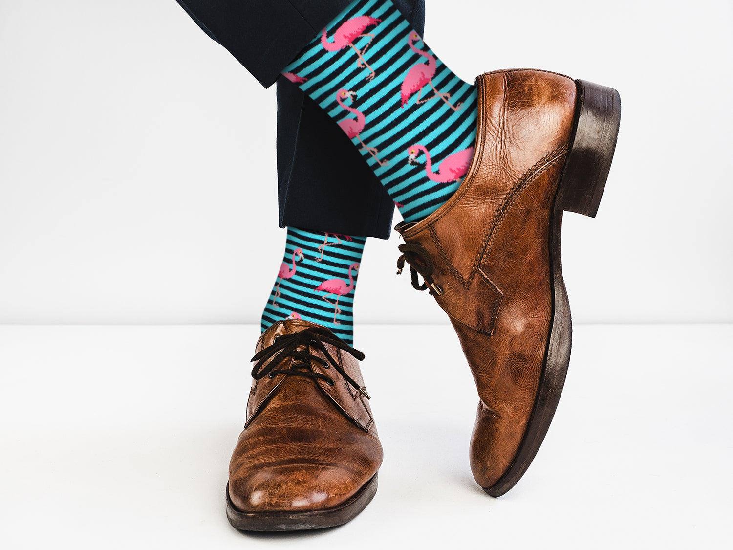 Brown dress shoes with striped socks featuring pink flamingos on a white background