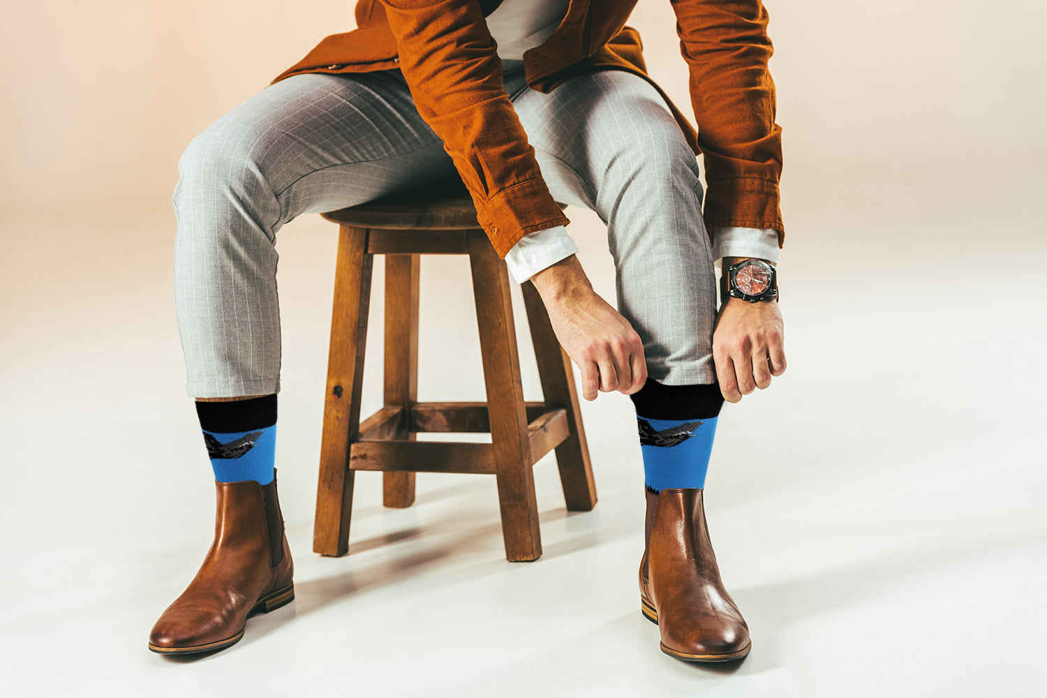 Person sitting on a stool wearing brown boots, gray pants, and blue socks with a blurred background.