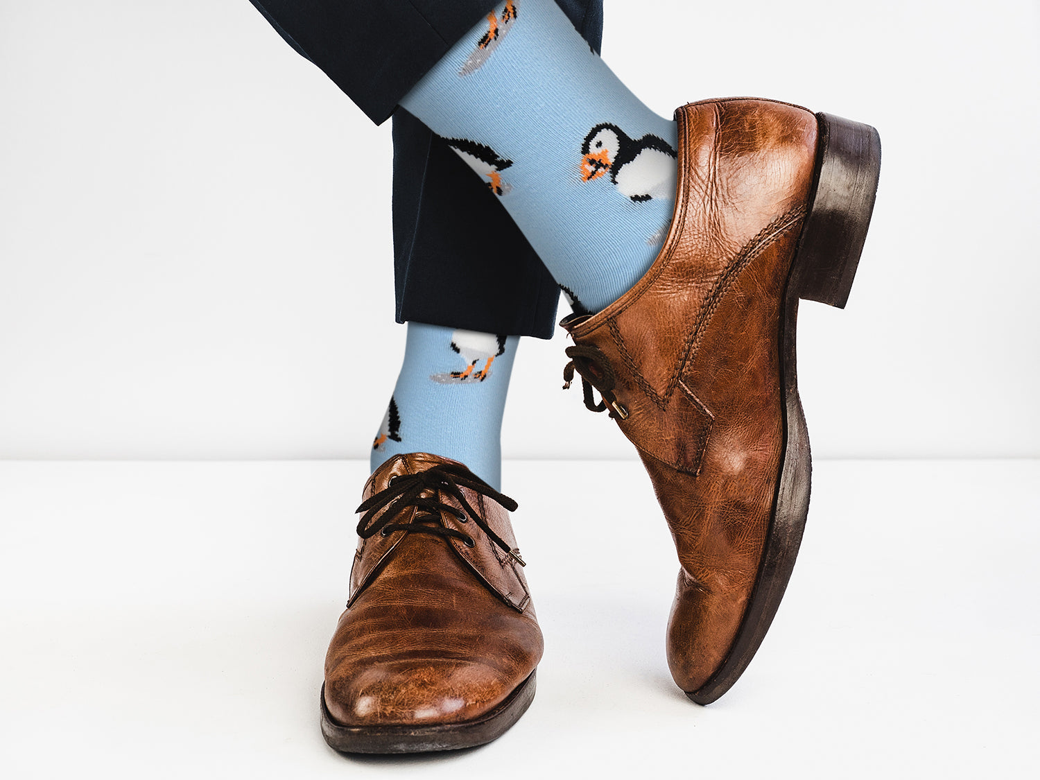 Blue socks with penguin design worn with brown leather shoes on a white background