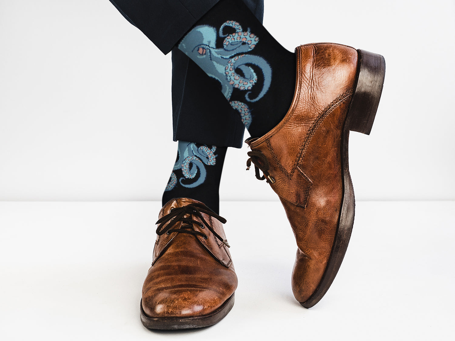 Brown dress shoes and black pants with blue patterned socks on a white background