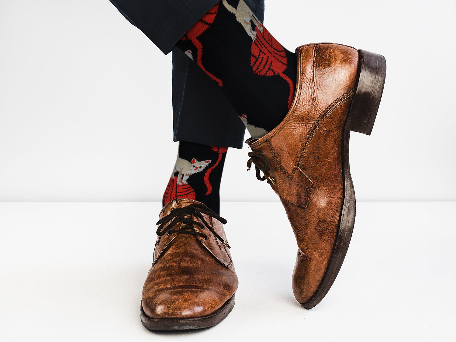 Brown leather shoes worn with patterned socks on a white background