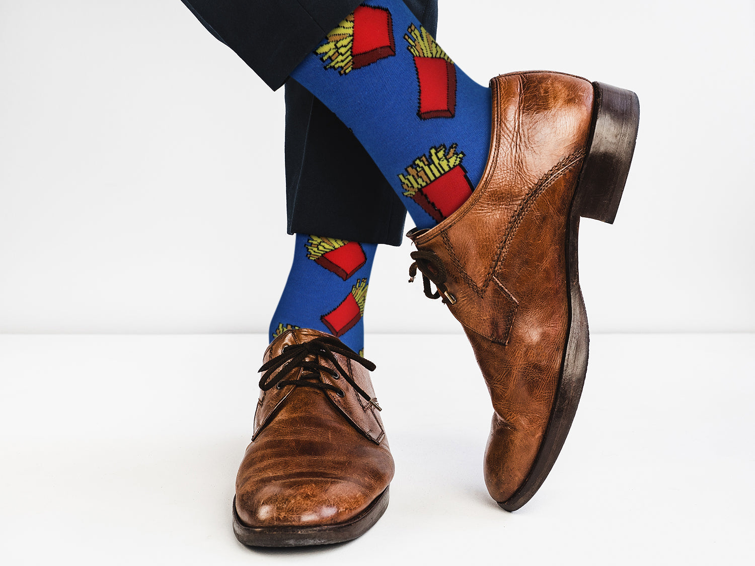 Brown dress shoes with blue socks featuring red and yellow patterns on a white background