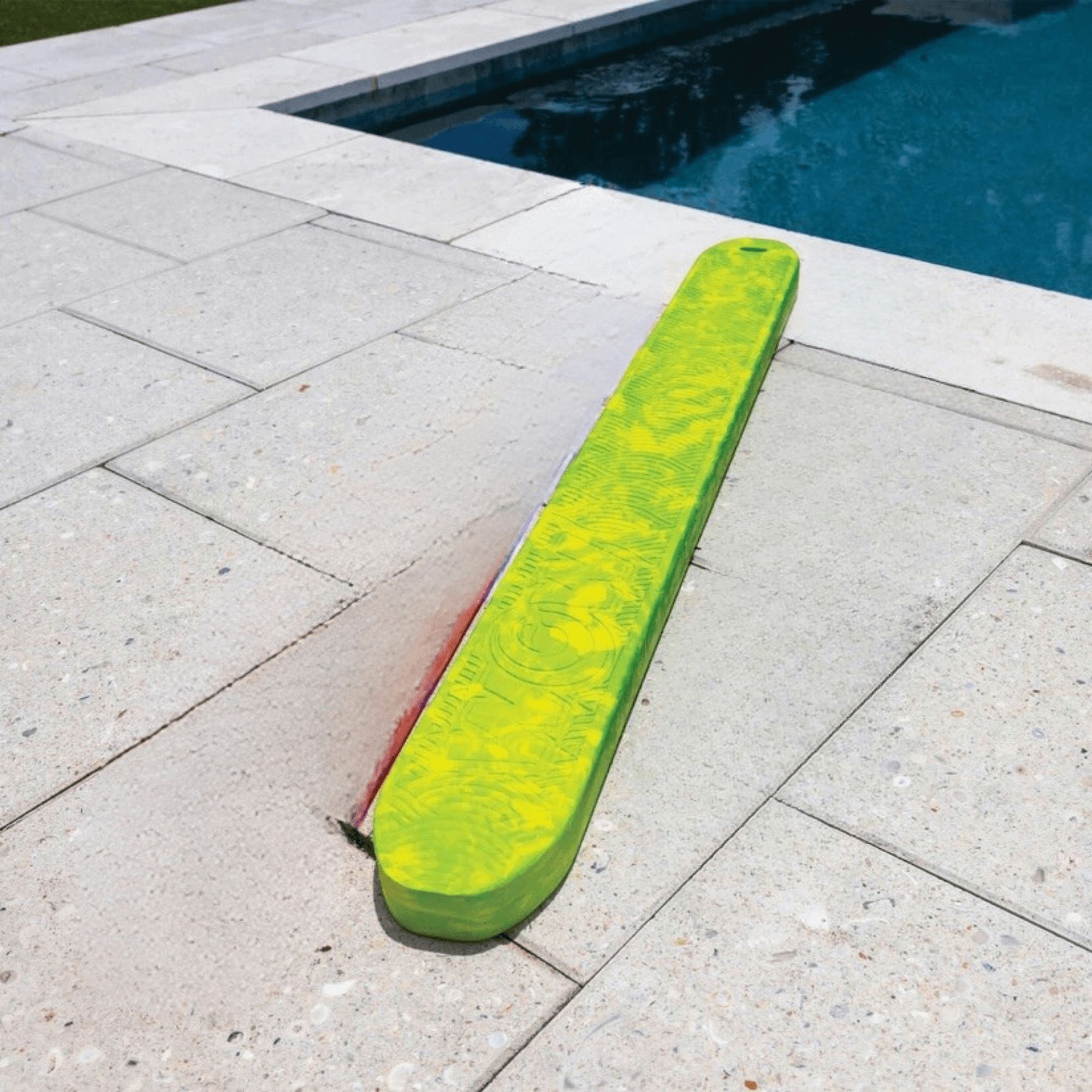 Green pool float on a concrete patio next to a pool