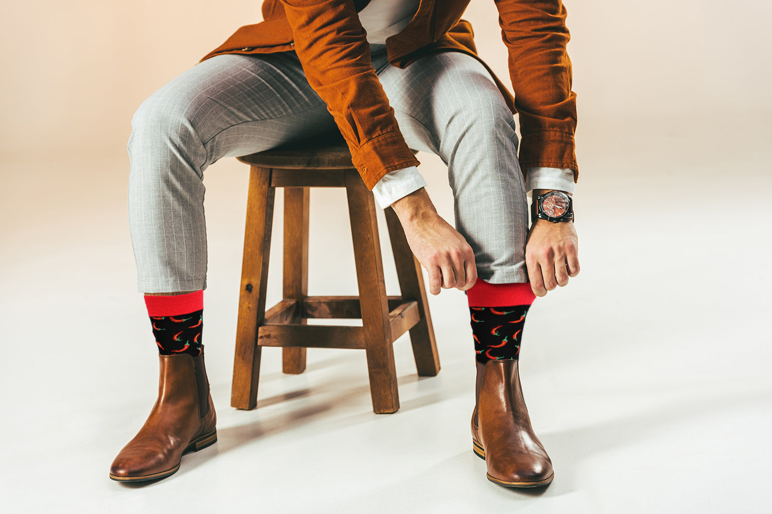 Person wearing brown boots, gray pants, and patterned socks sitting on a wooden stool.
