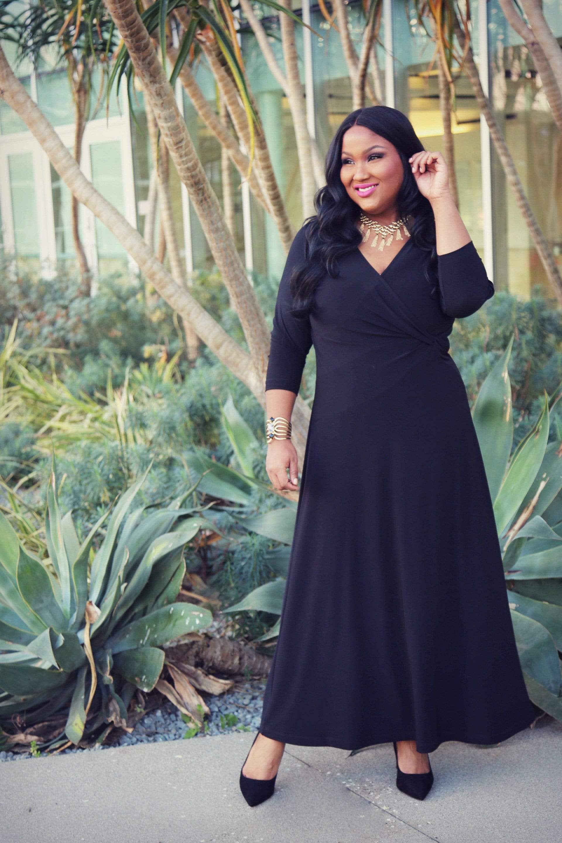 Woman in a black dress standing outdoors with plants in the background