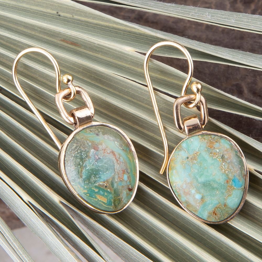 Gold-framed turquoise stone earrings on a textured surface
