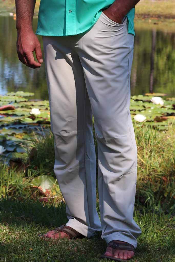 Person wearing light gray pants and a turquoise shirt standing in a natural setting with water and plants.