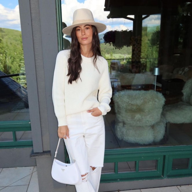 Woman in a white outfit with a hat standing in front of a store window.