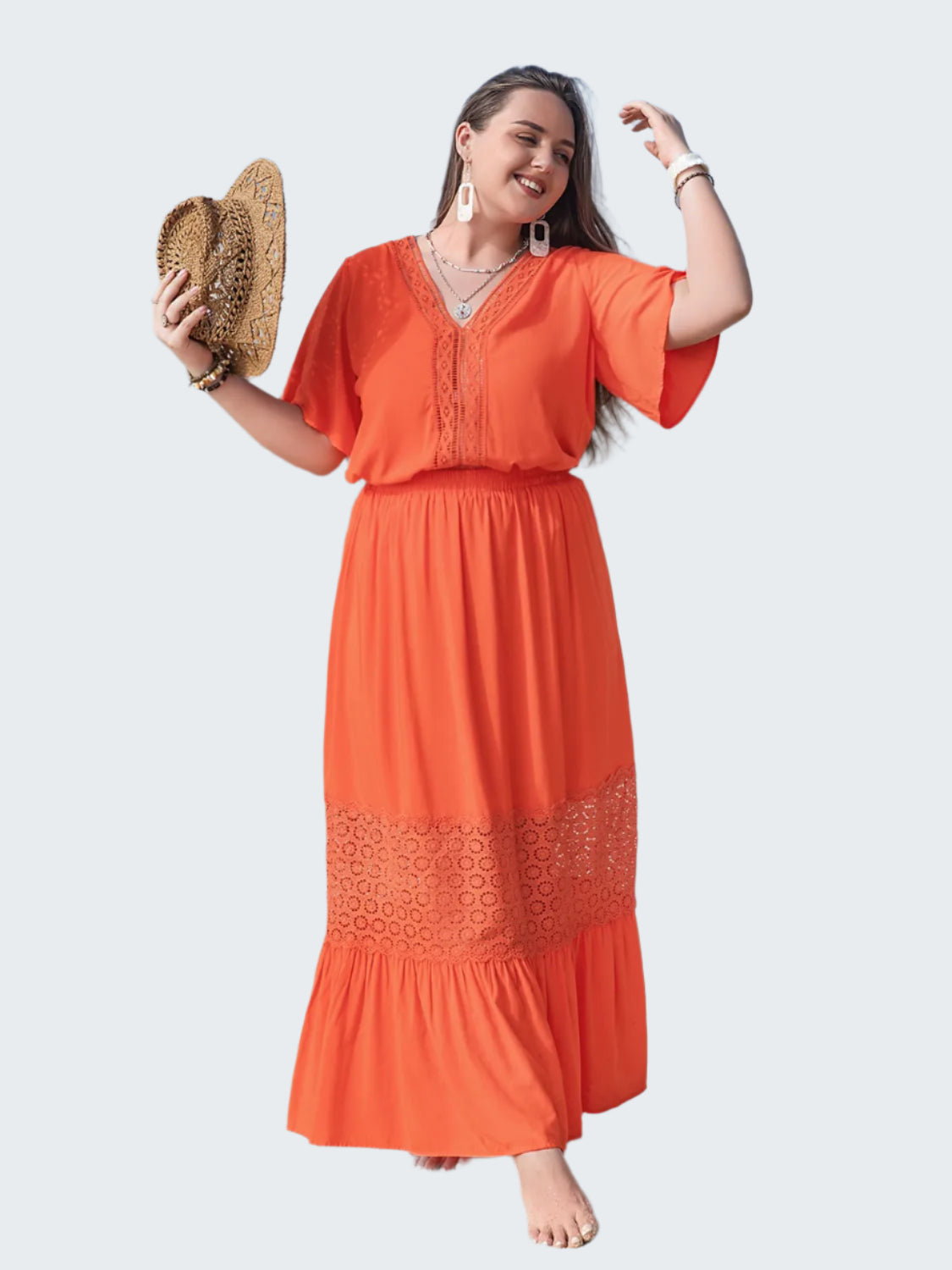 A woman standing on a beach wearing an orange maxi dress with lace details and flutter sleeves.