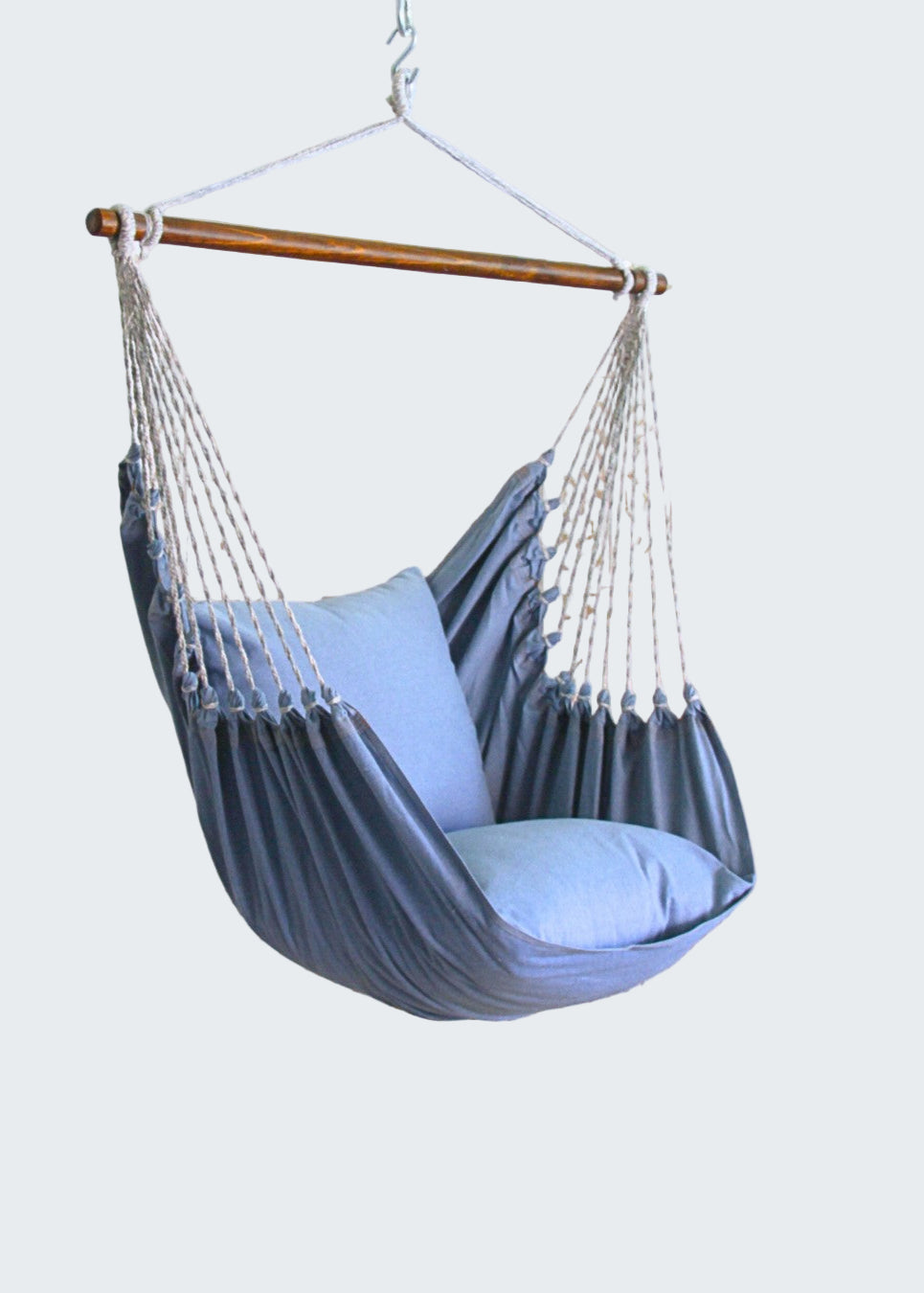 Gray hammock chair with blue pillow hanging indoors next to a plant.
