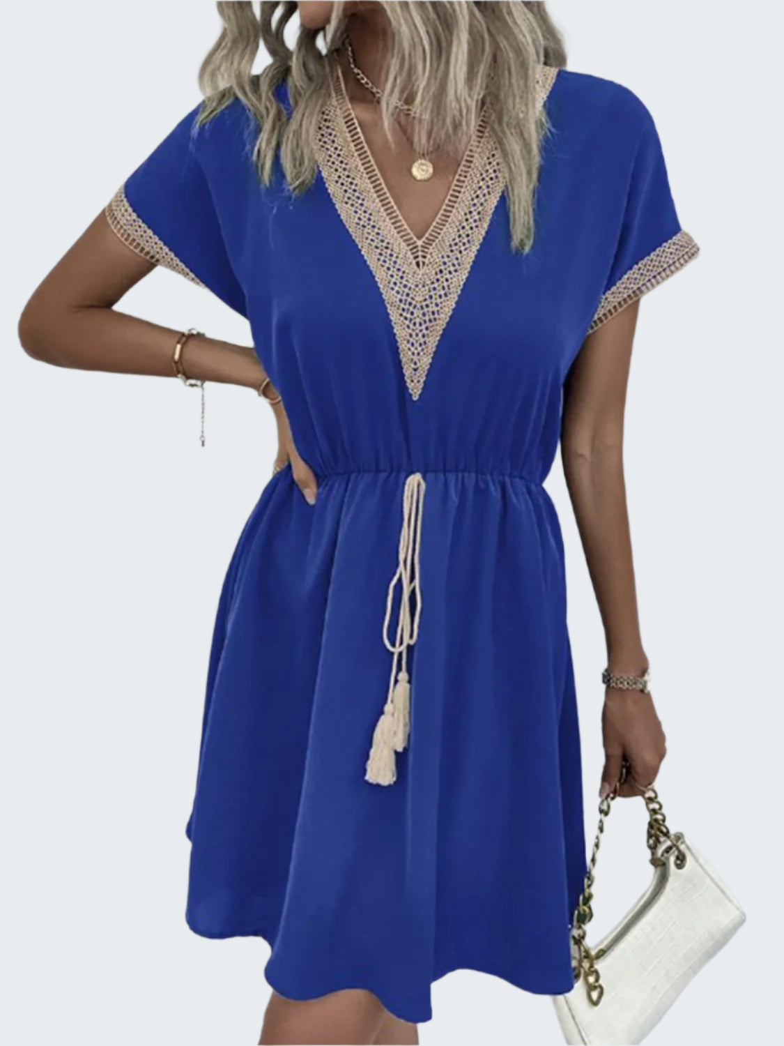 A model wearing a blue v-neck short sleeve dress with tassel detailing, paired with a white accessory.