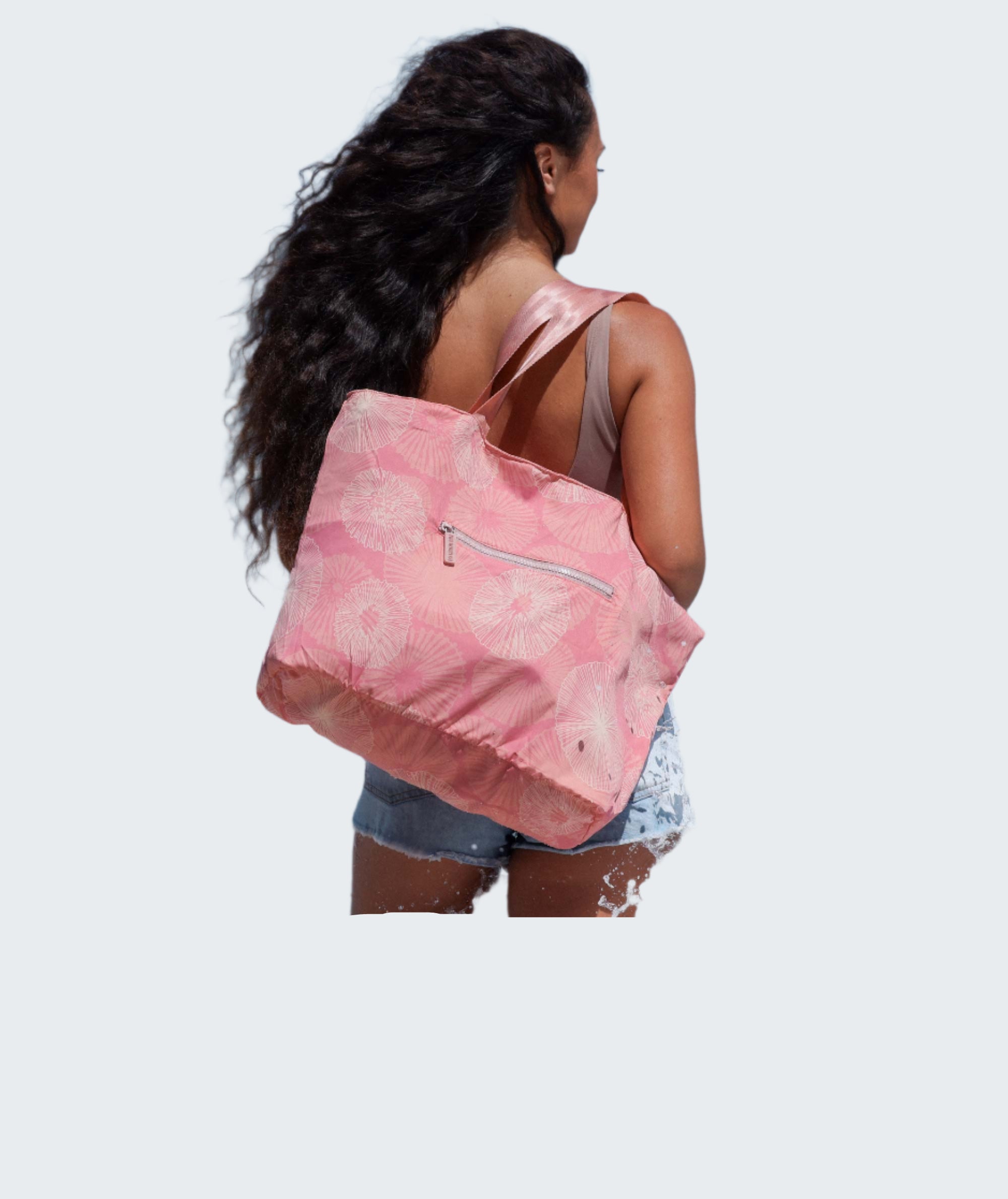 Woman with a pink tote bag walking along a beach