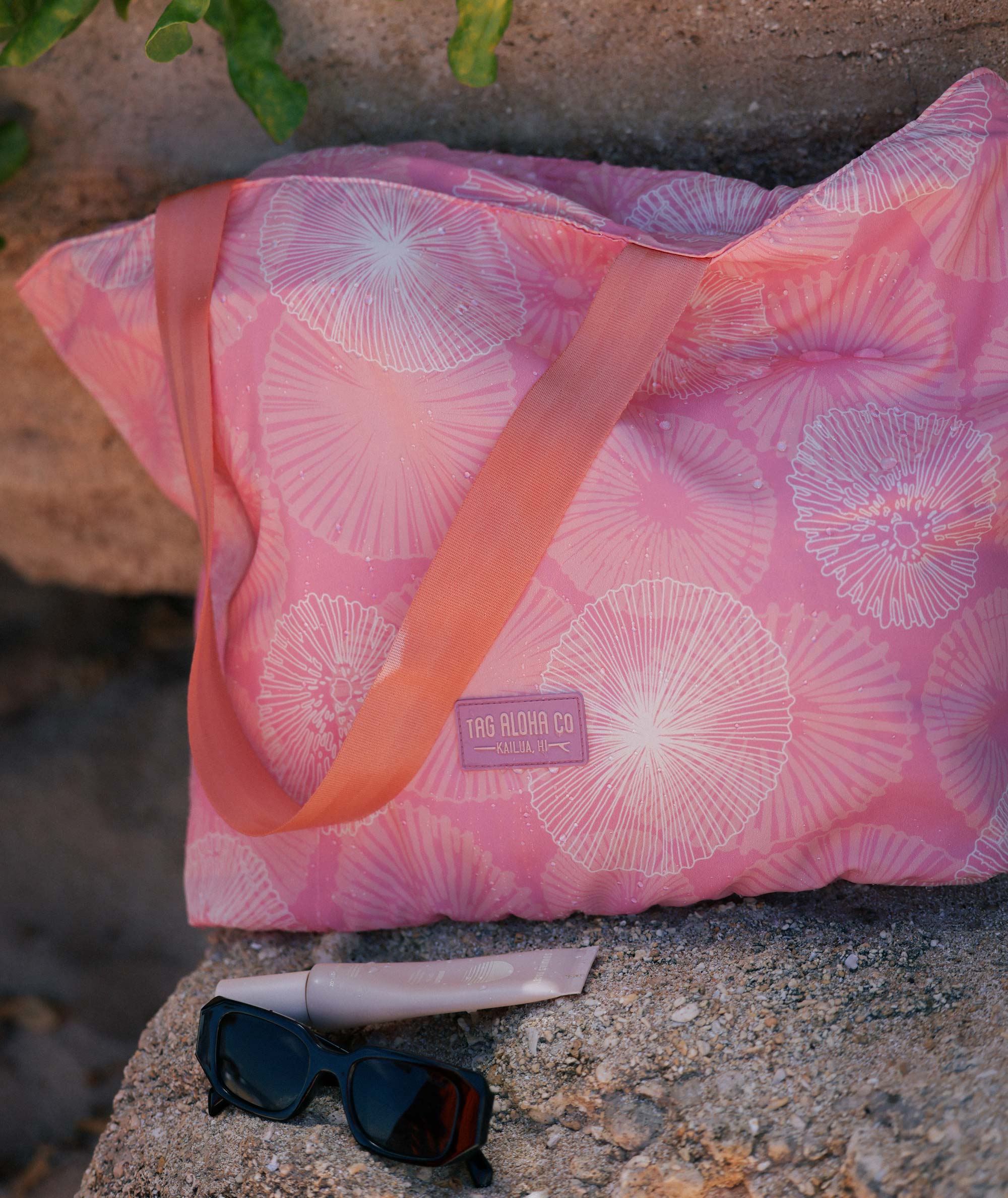Pink patterned bag with sunglasses on a stone surface