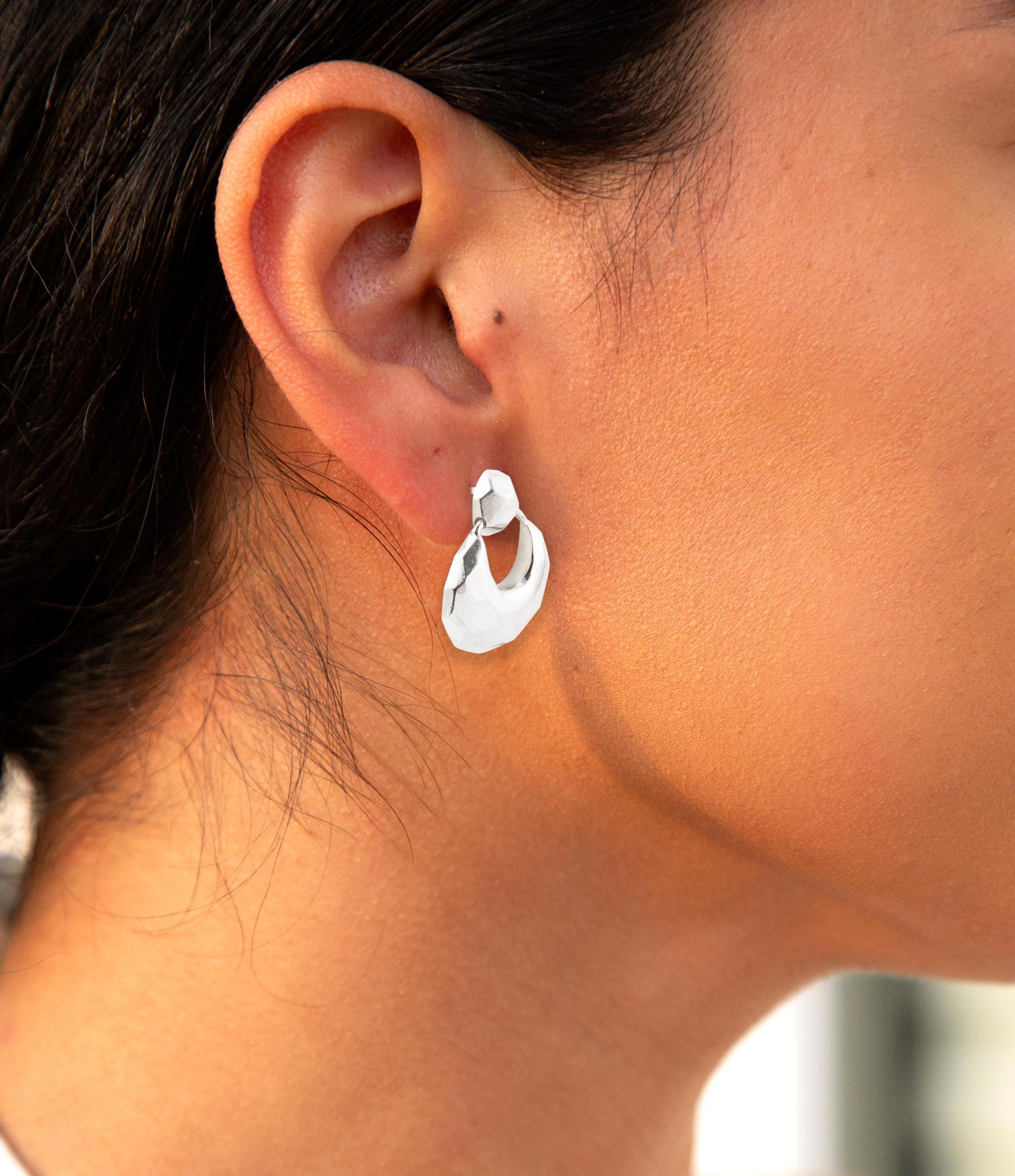 Close-up of a person wearing a silver hoop earring with a blurred background