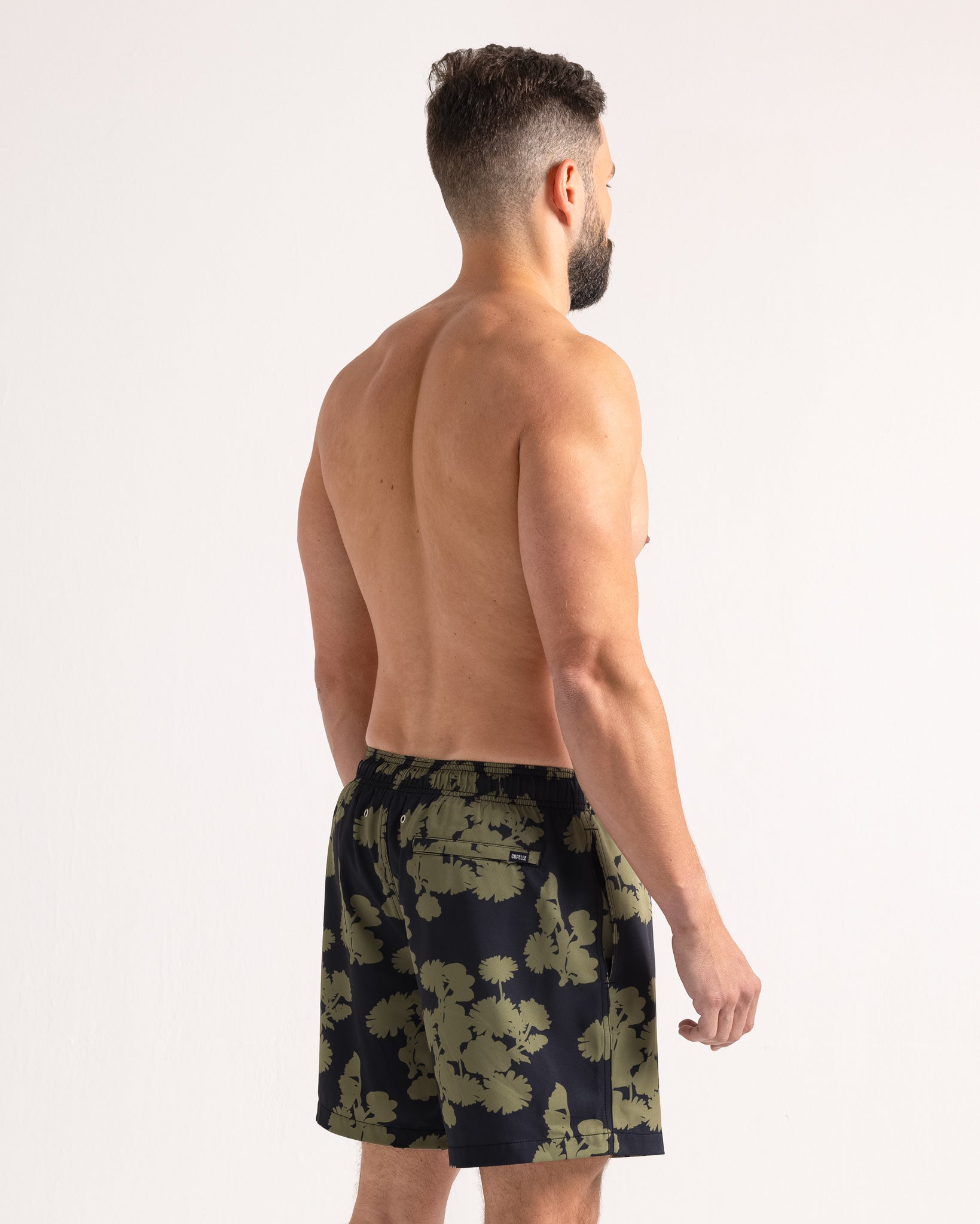Man wearing black swim shorts with green floral pattern on a white background