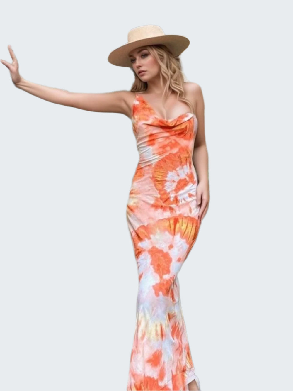 A woman wearing a backless, asymmetrical tie-dye maxi dress with a hat, standing in front of a rustic door.