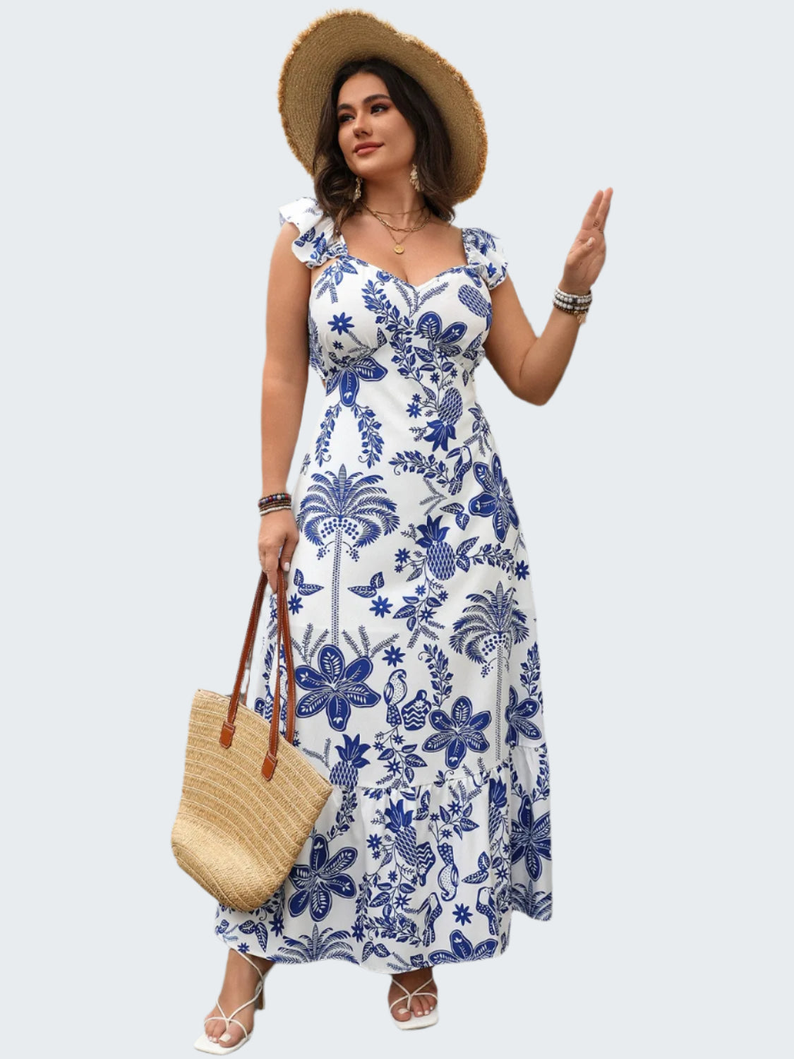 A woman wearing a plus size maxi dress with a blue floral pattern, featuring a sweetheart neckline and ruffled sleeves. She is accessorized with a straw hat, a wristwatch, and carrying a straw tote bag.
