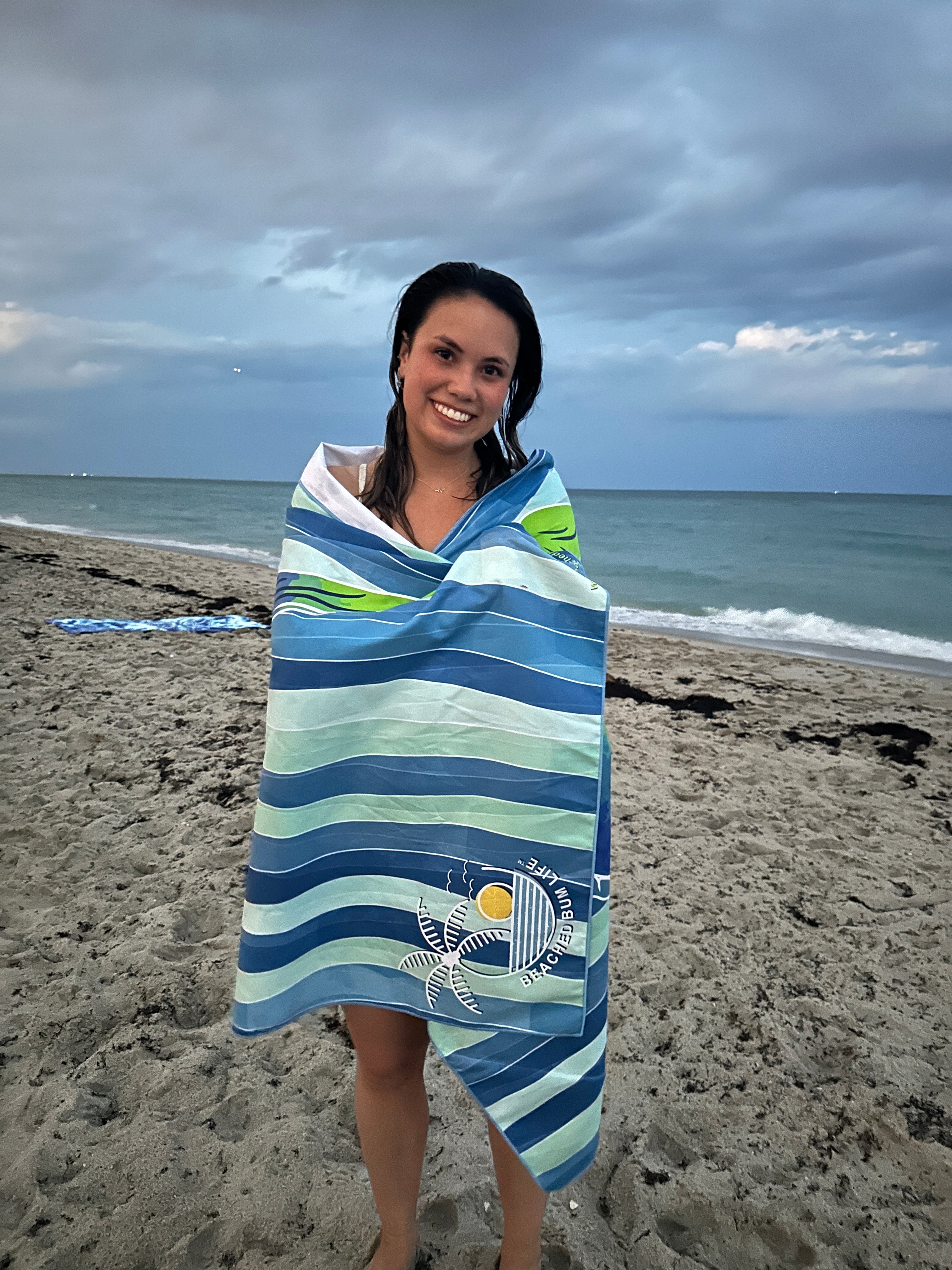 Woman wrapped in a striped beach towel on a sandy beach with ocean and sky in the background