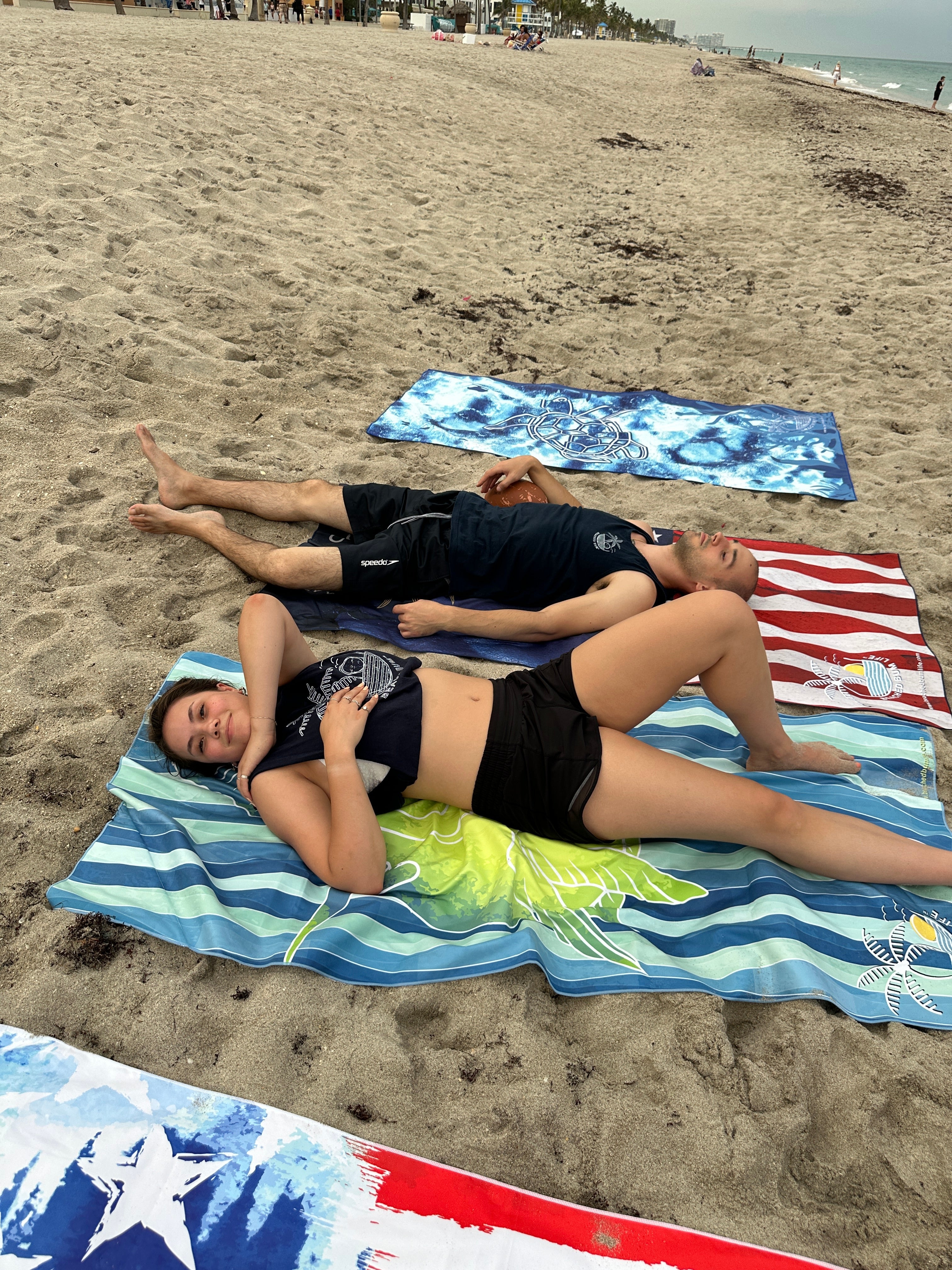 Two people lying on colorful beach towels on a sandy beach with ocean in the background