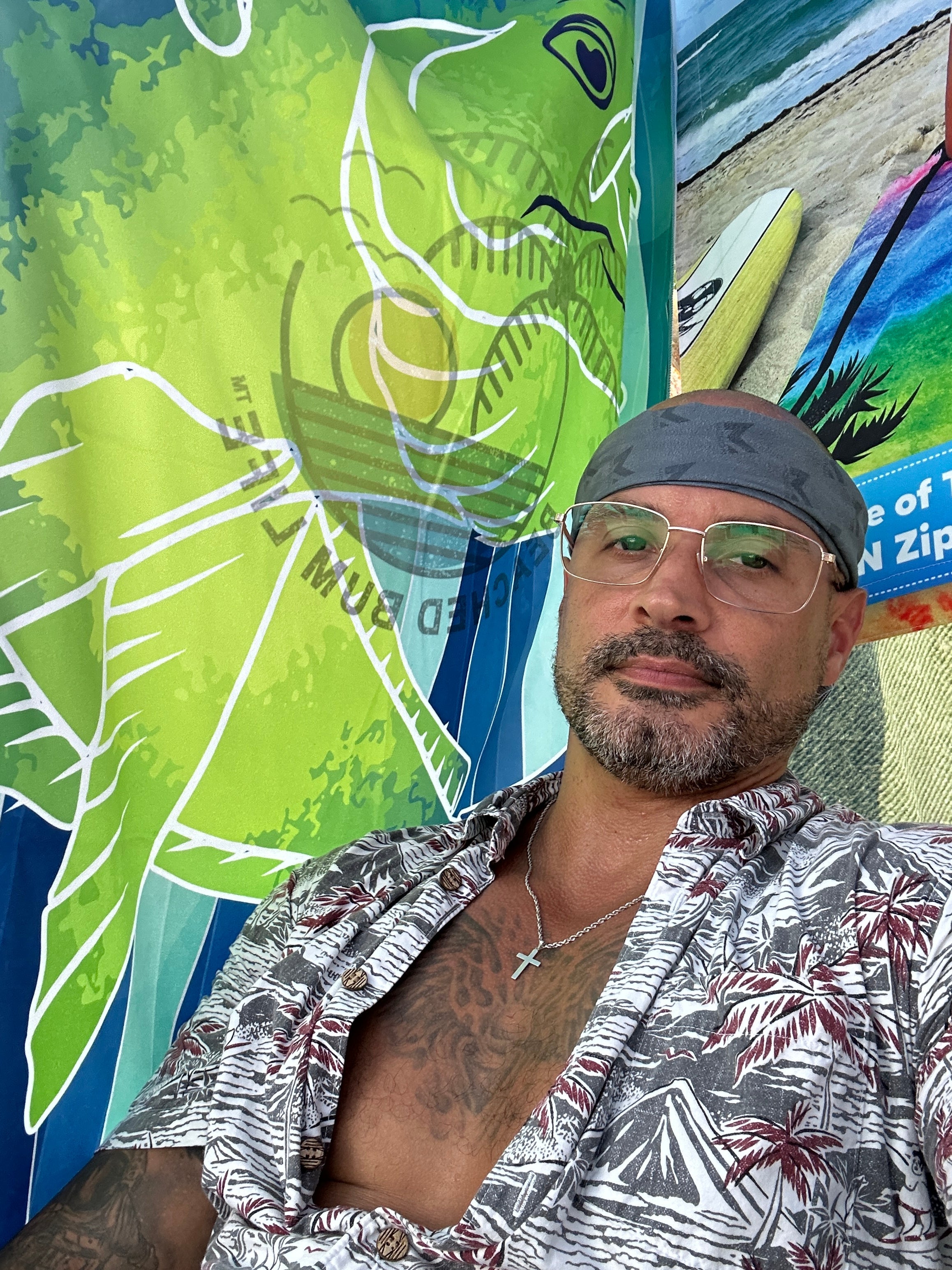 Man wearing a patterned shirt and headband in front of a colorful mural of a fish and beach scene.