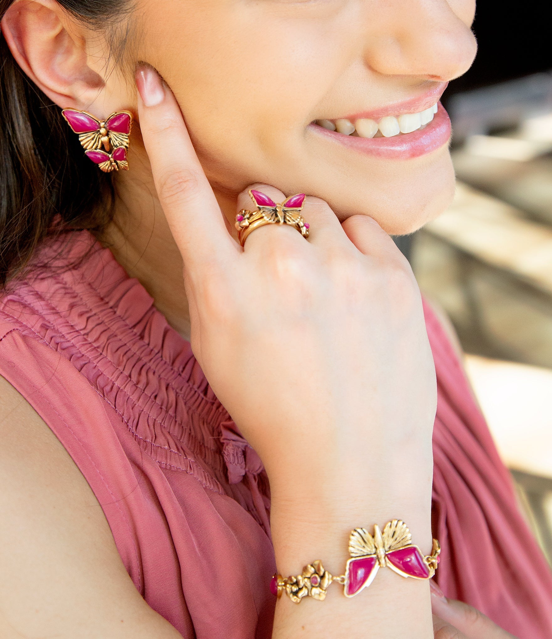 Woman wearing pink butterfly-themed jewelry including earrings, ring, and bracelet.