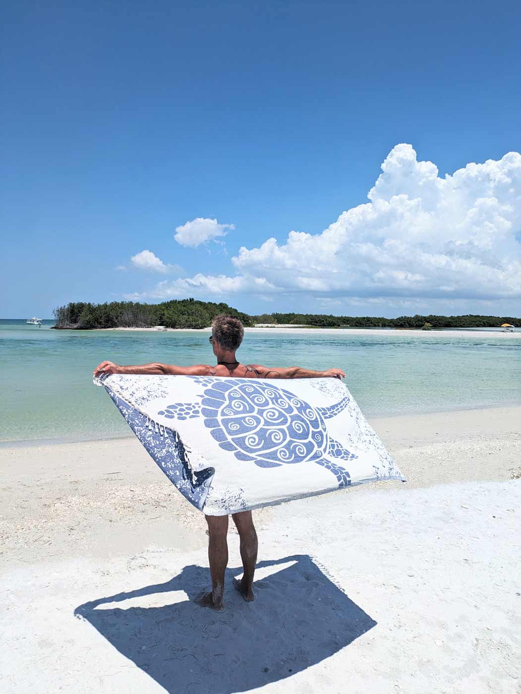Person holding a towel with a turtle design on a tropical beach