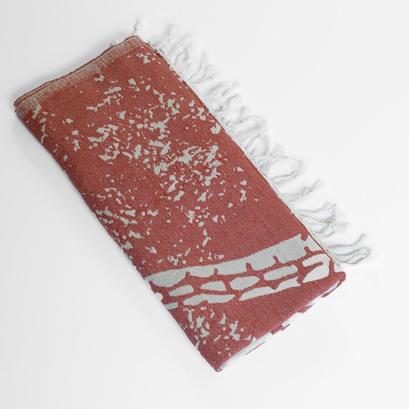 Red towel with white speckles and frayed edges on a light gray background