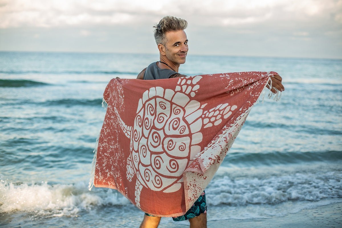 Man holding a red and white towel with a turtle design on a beach