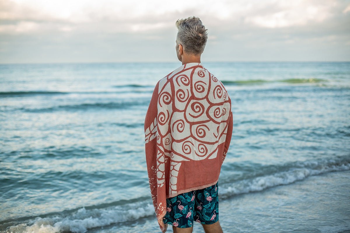 Person standing on a beach with a patterned towel draped over their shoulders