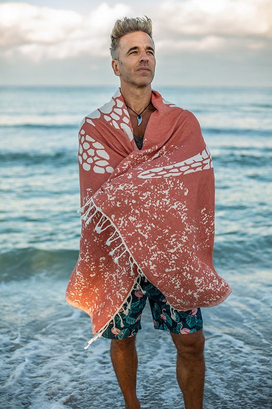 Man standing on a beach with a pink towel draped over his shoulders