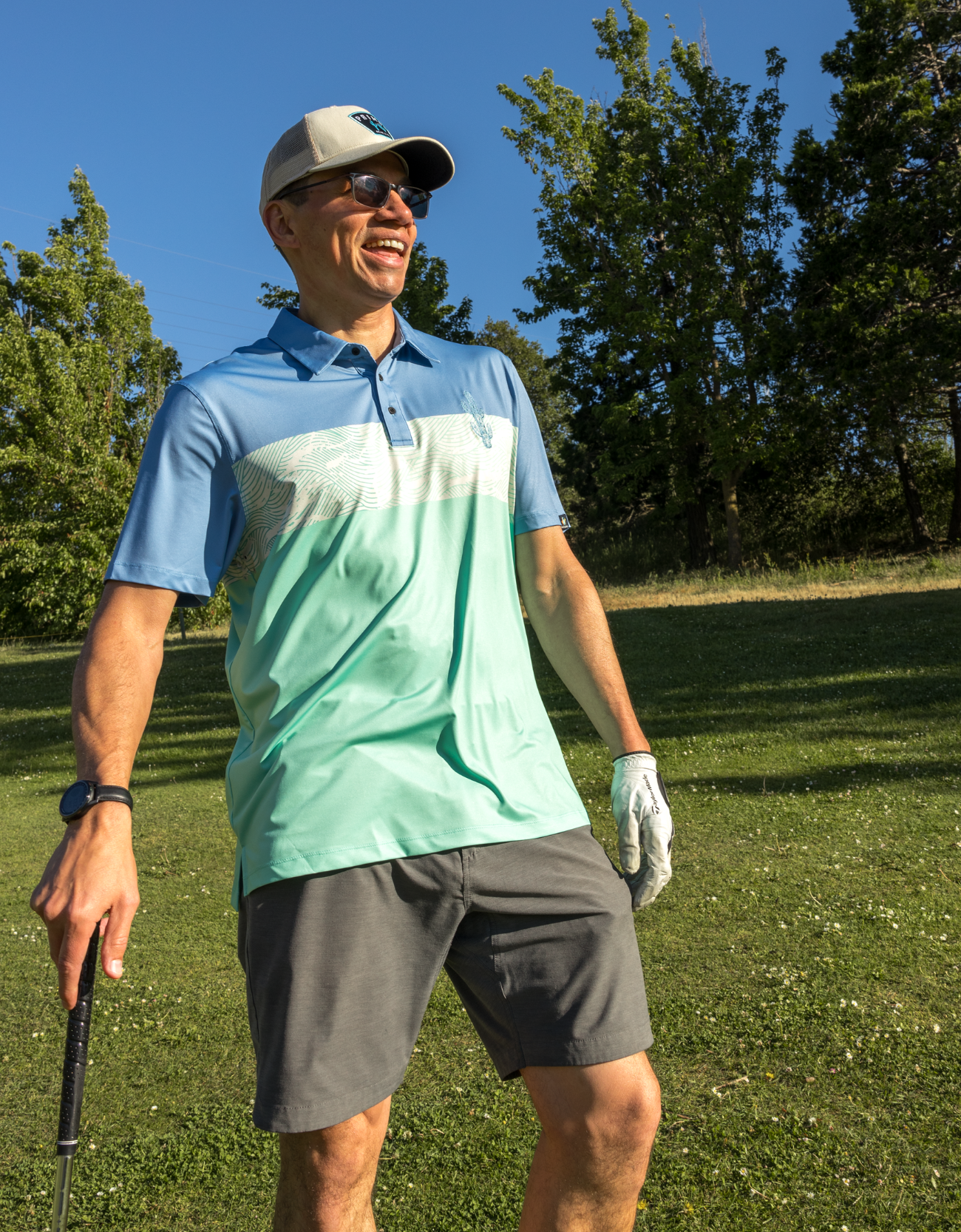 Man in a blue and green gradient shirt and gray shorts standing on a golf course.