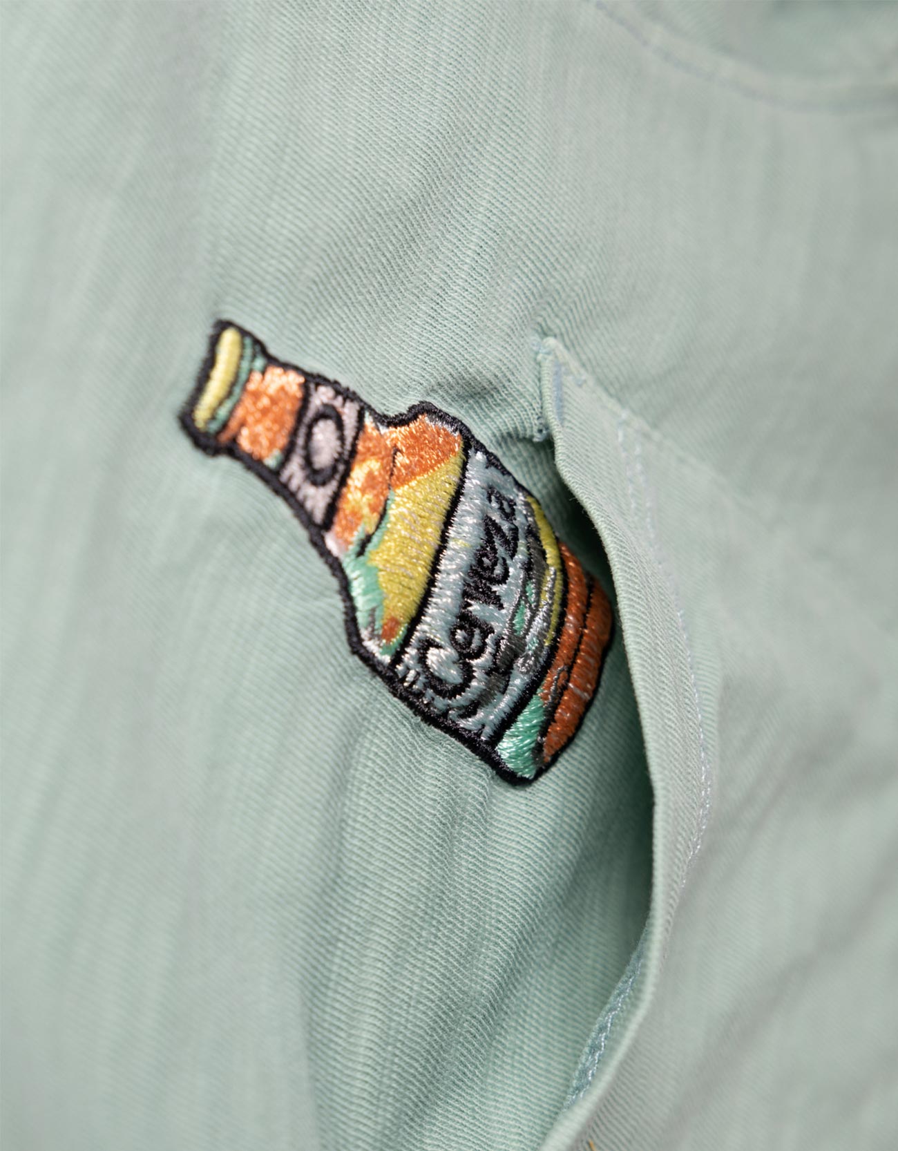 Embroidered bottle patch on a light green shirt