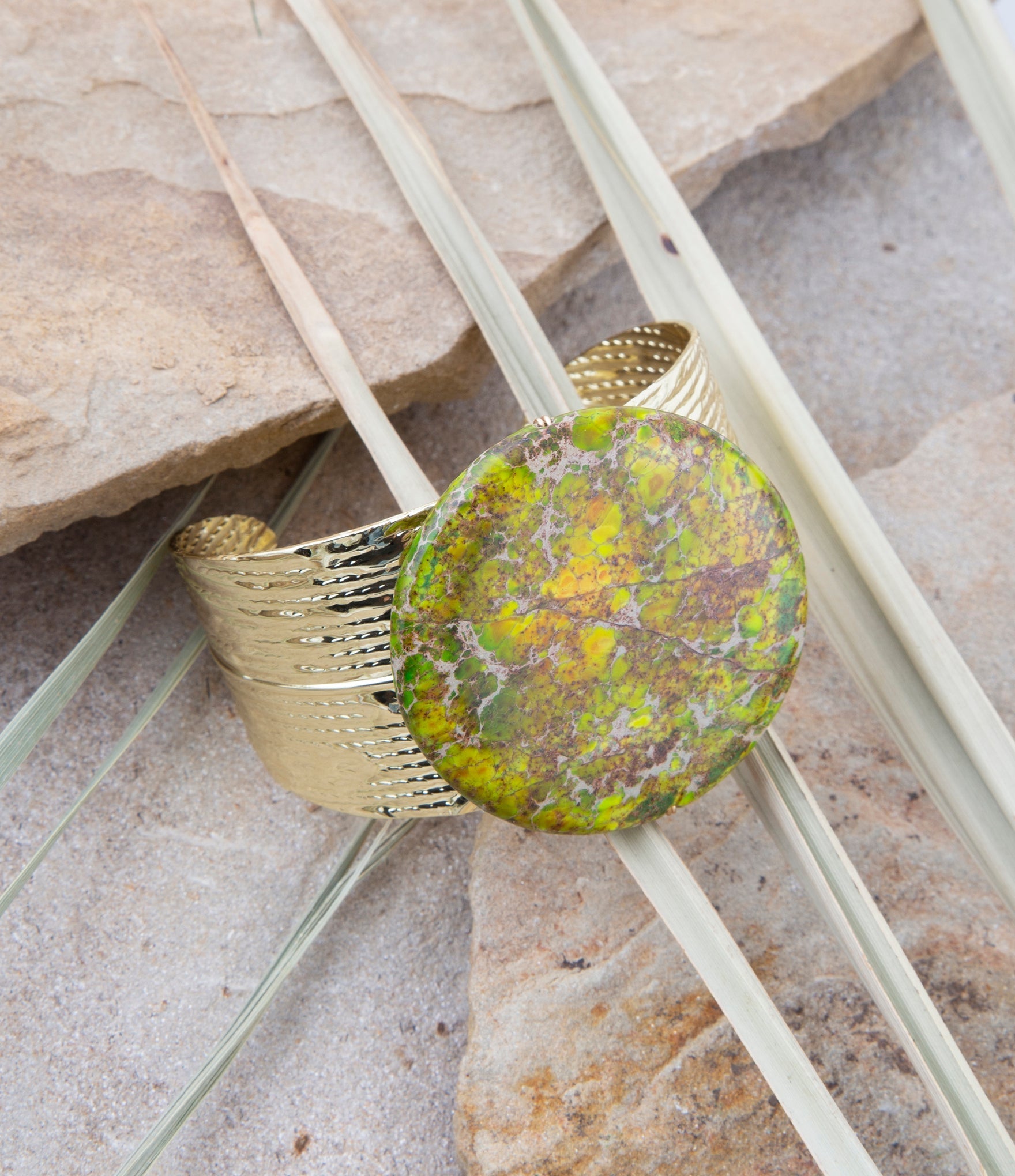Gold bracelet with a green stone on a natural stone background