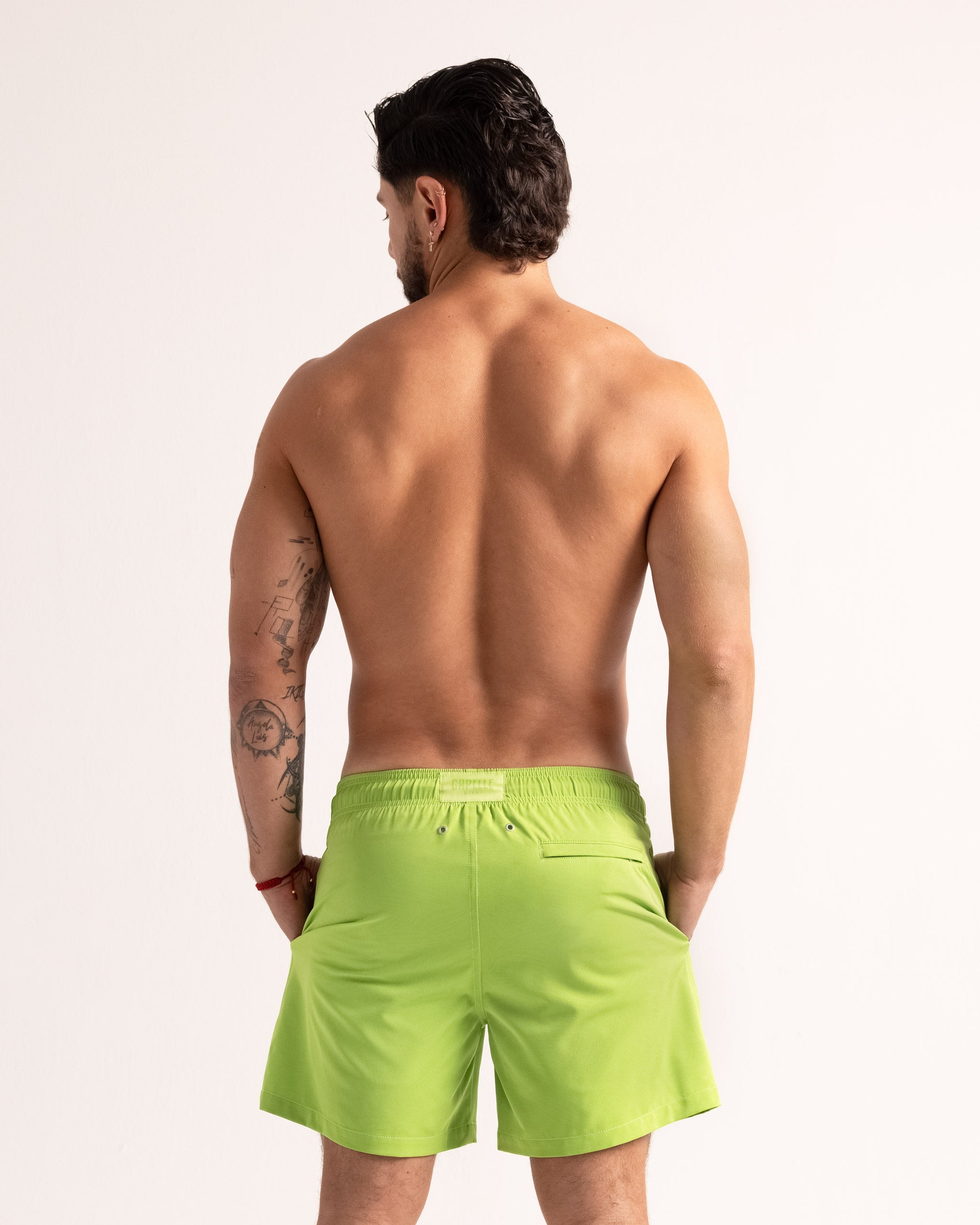 Man wearing bright green swim shorts on a plain background