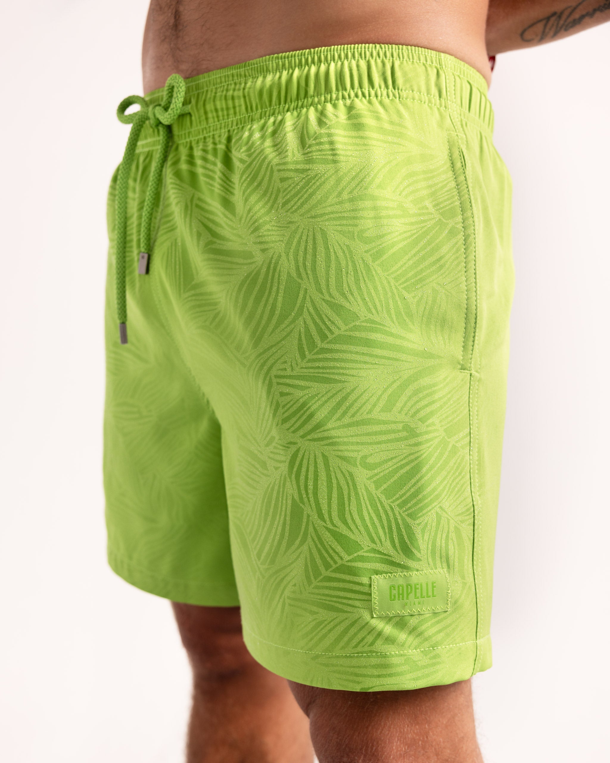 Green leaf-patterned swim shorts on a white background