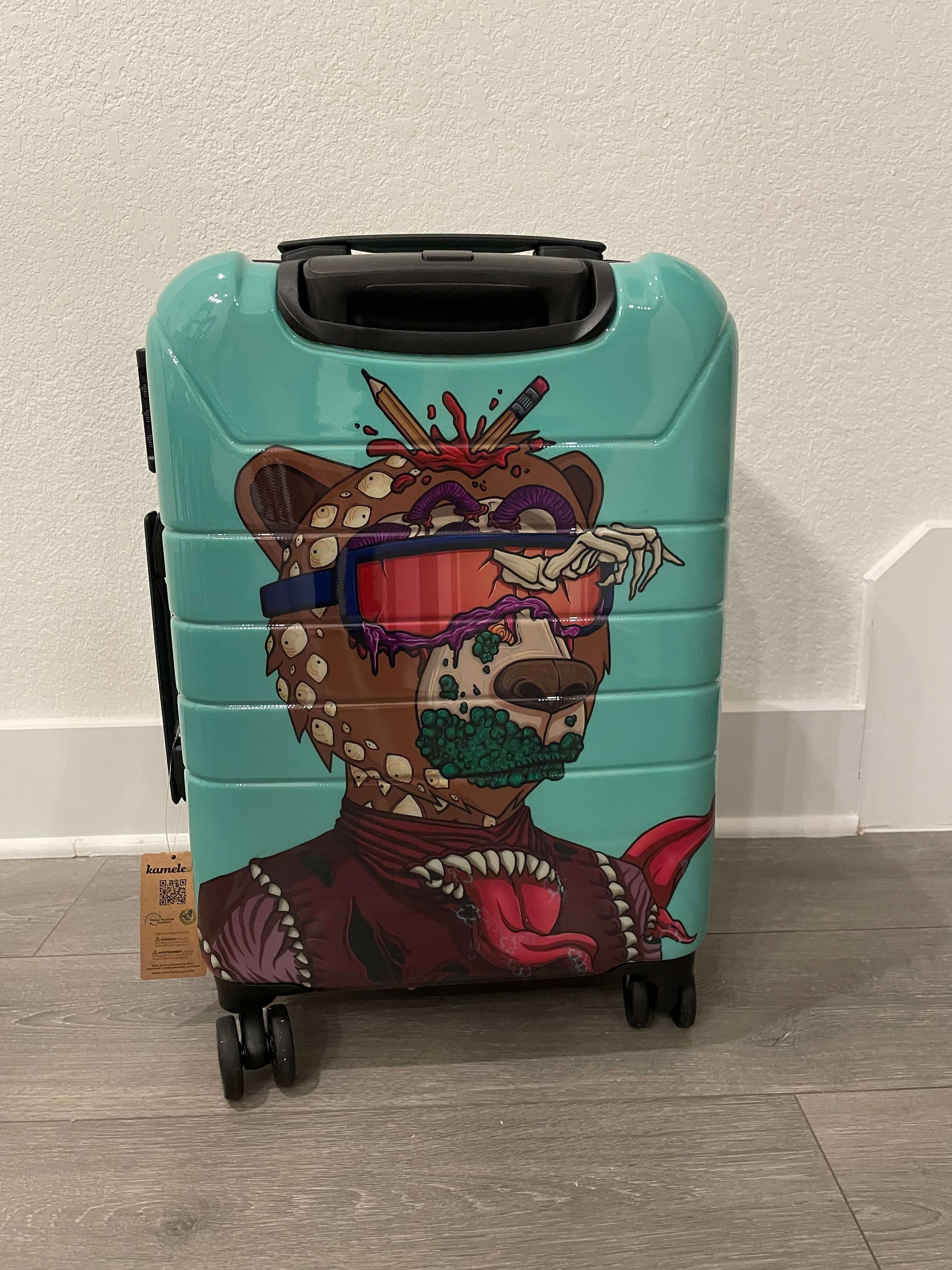Turquoise suitcase with a colorful bear design on a light wooden floor.