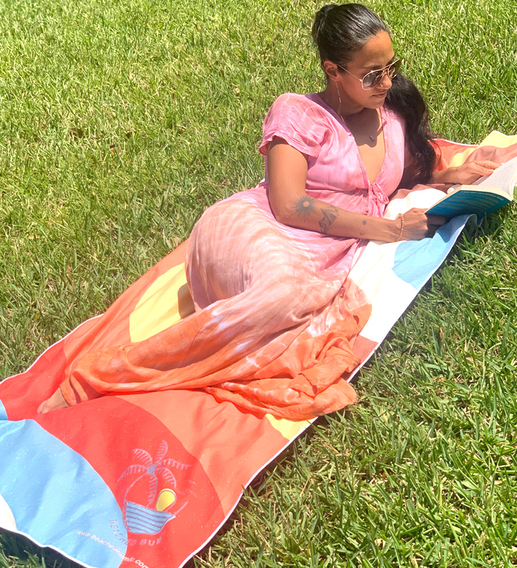 Woman in a pink dress lying on a colorful towel in the grass