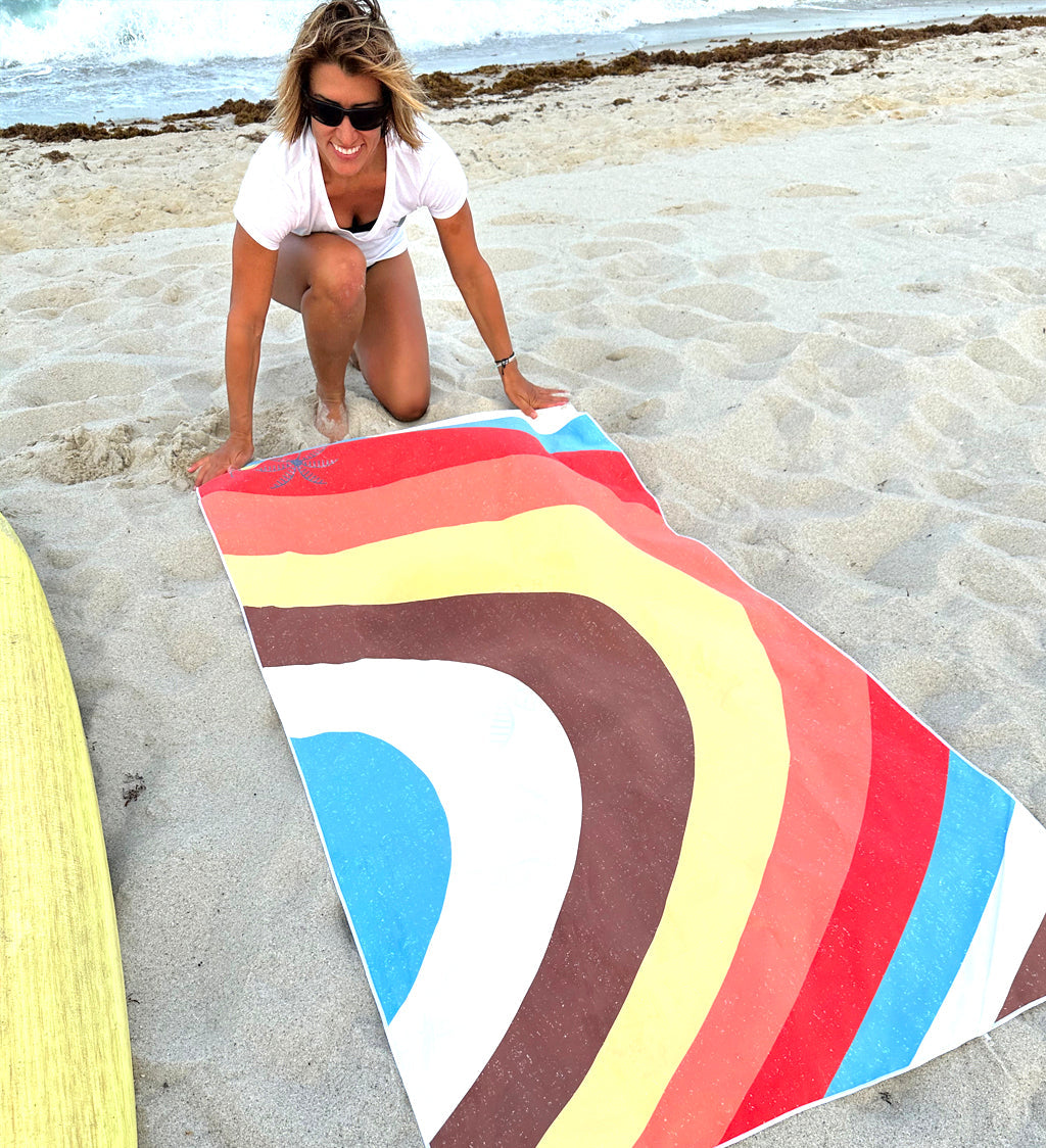 Woman setting up a colorful beach towel on a sandy beach.