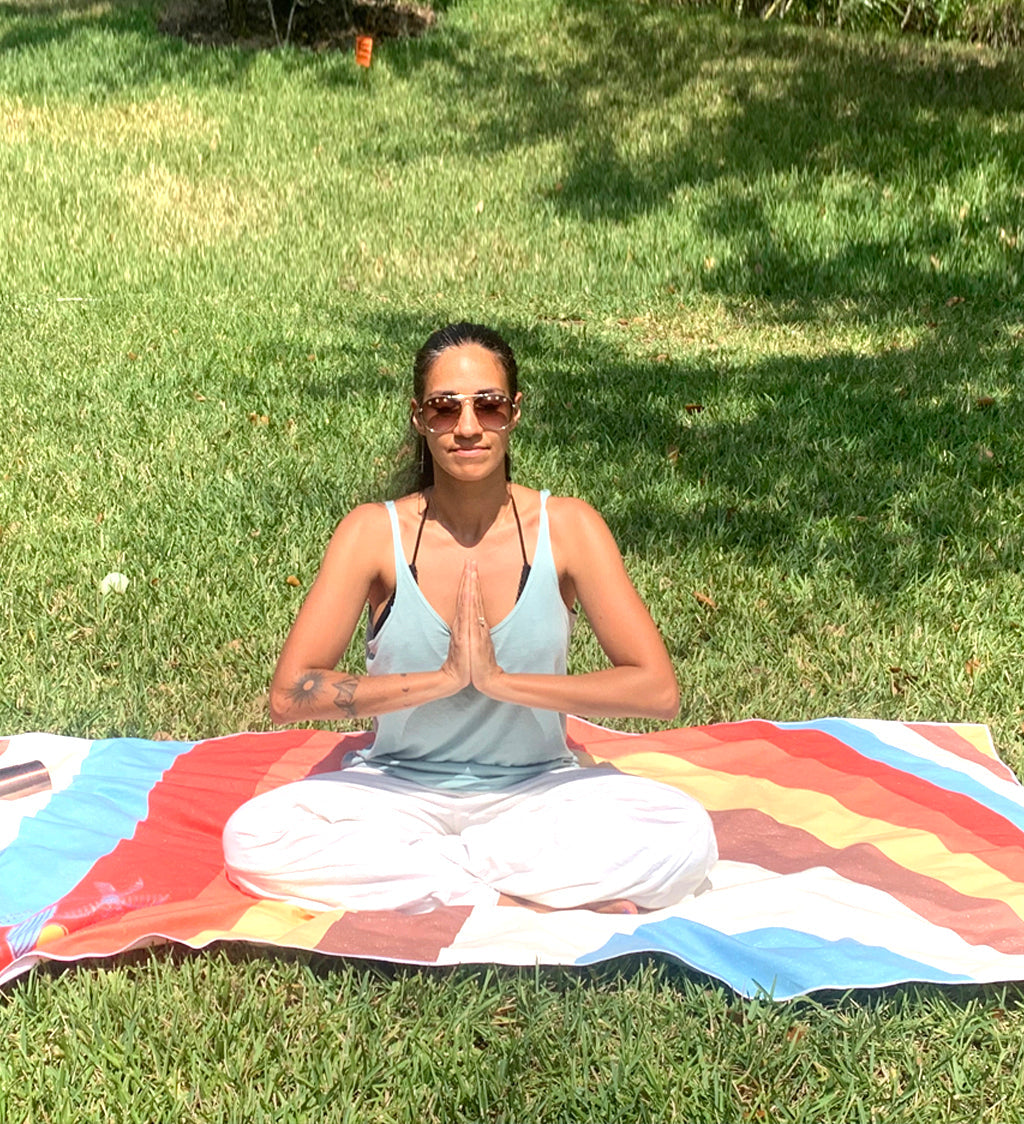 Woman meditating on a colorful mat in a grassy area