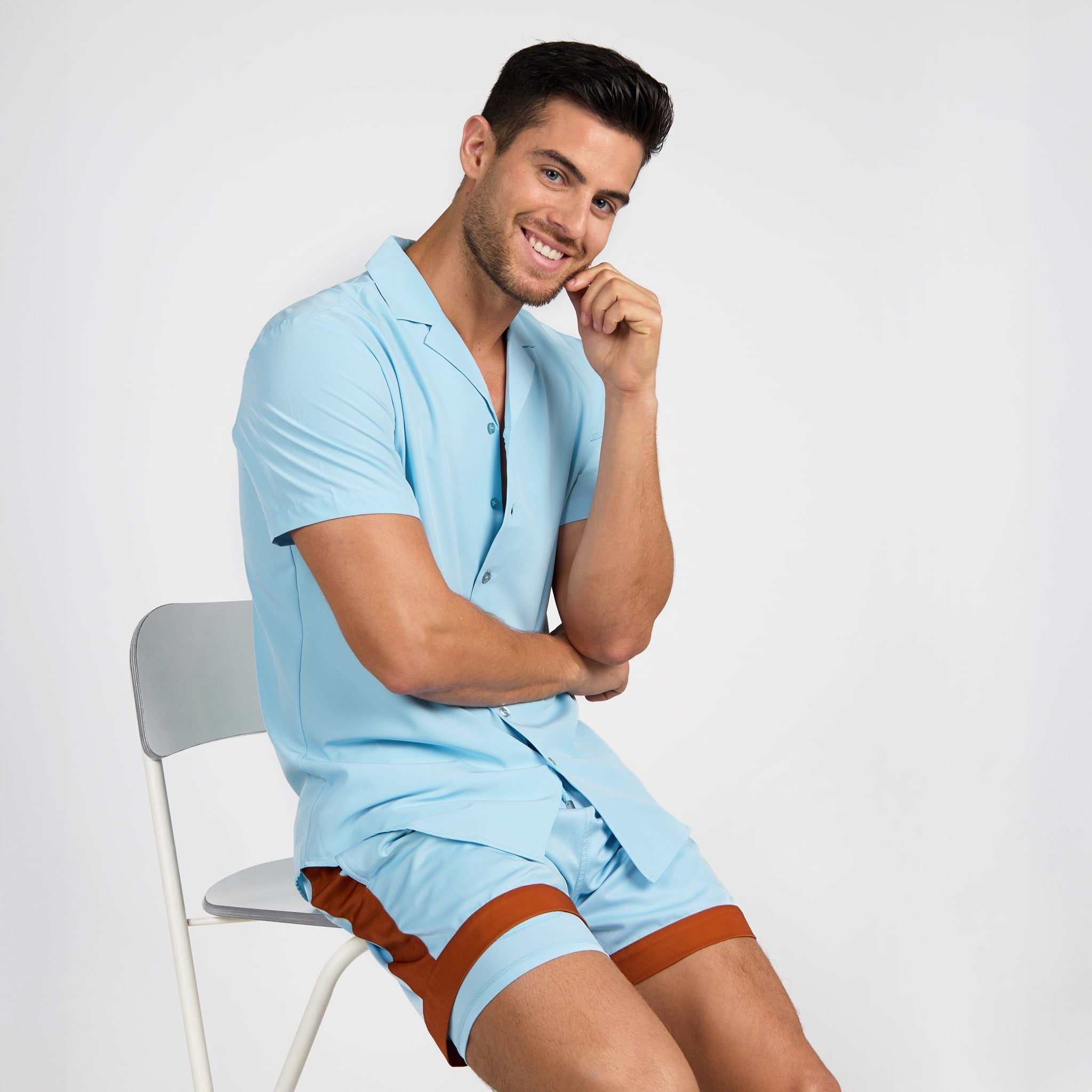Man wearing a light blue outfit sitting on a chair against a white background