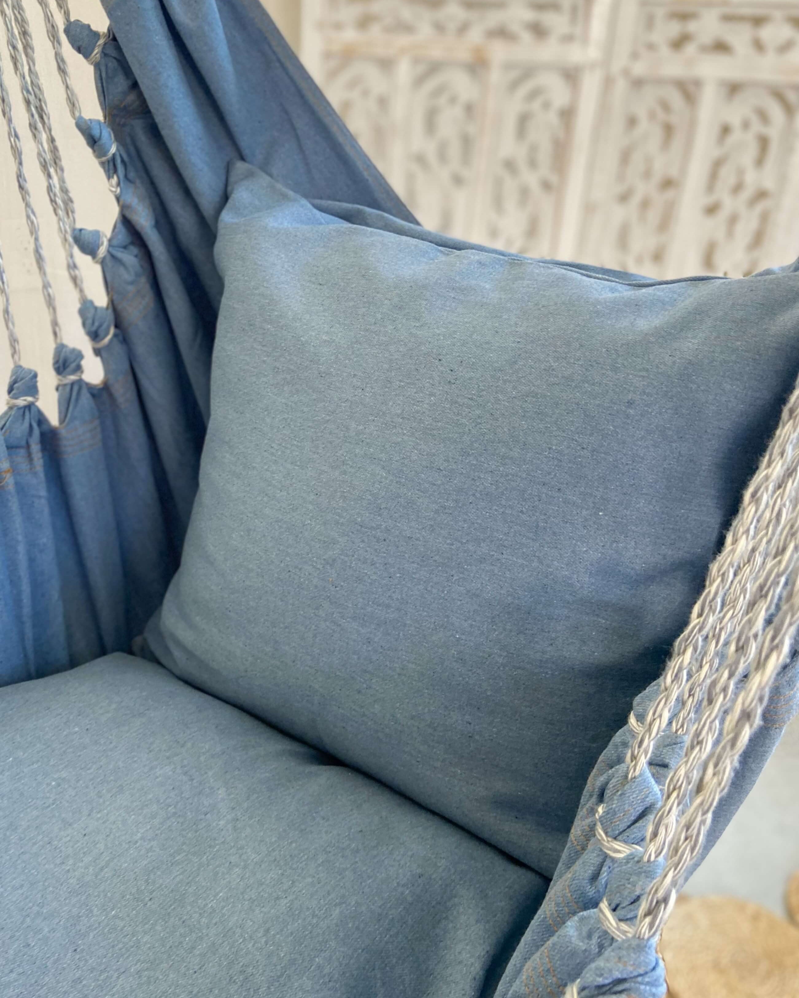 Blue hammock chair with a pillow against a textured wall background