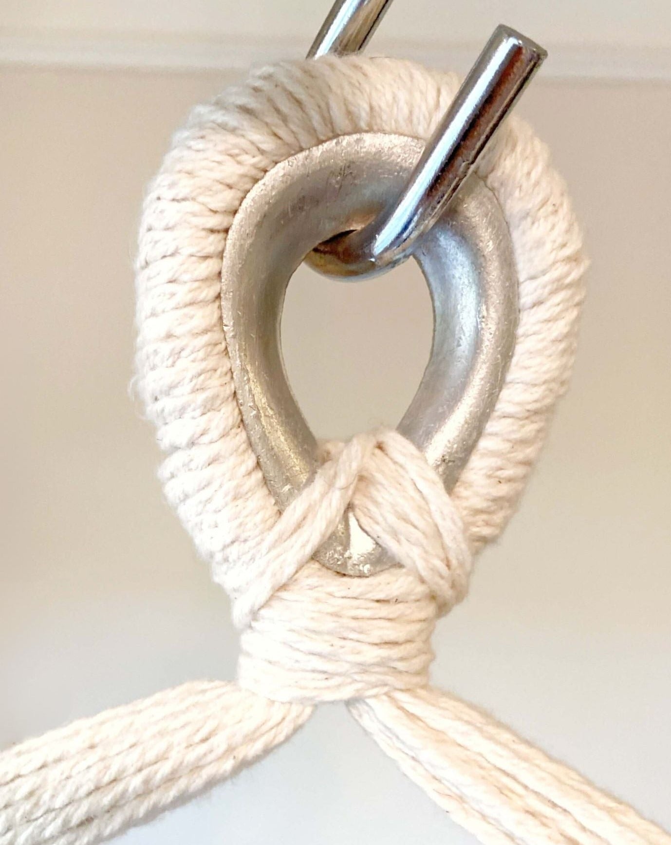 Close-up of a metal hook with a white rope tied around it on a light background