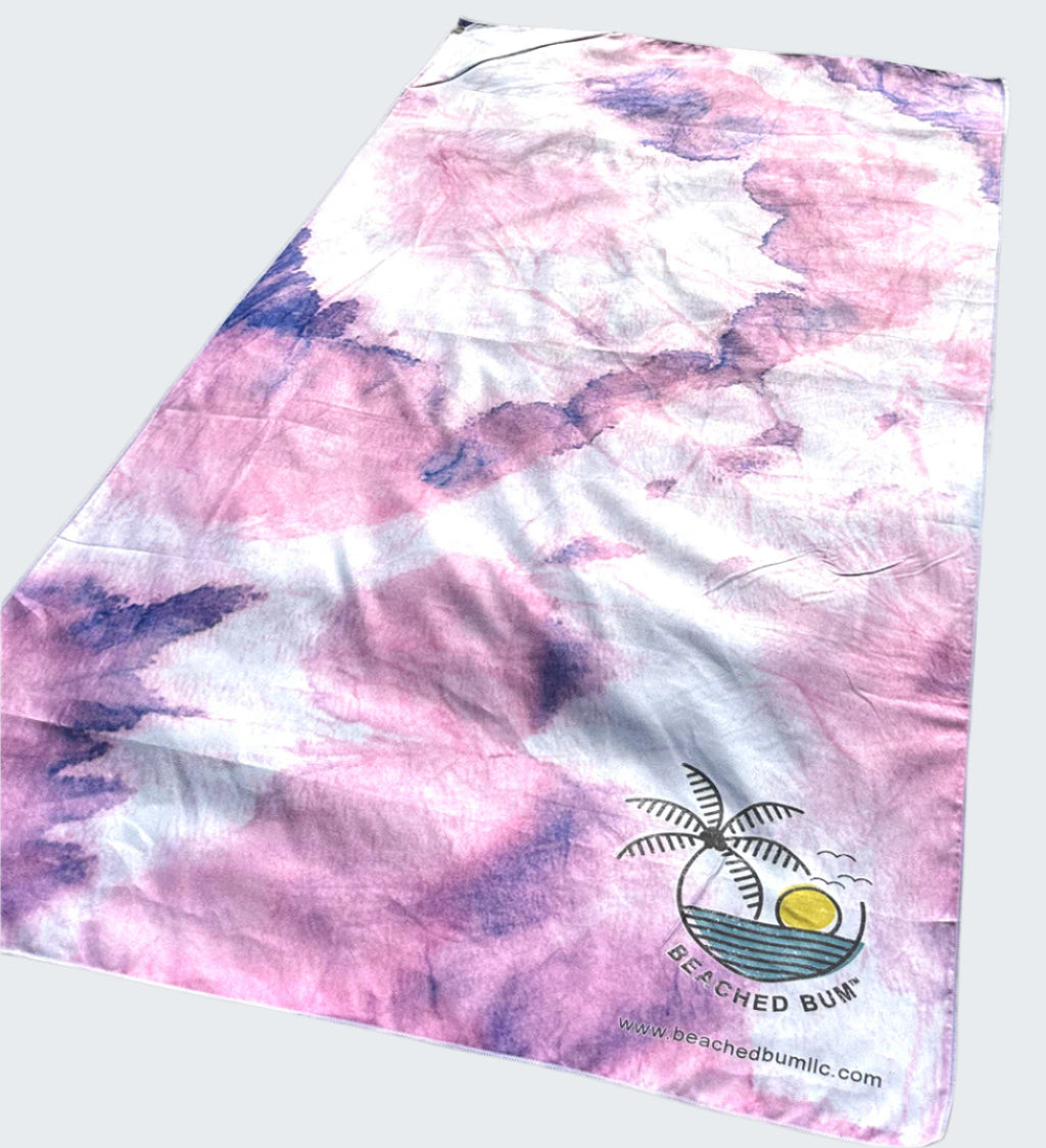 Pink and purple tie-dye towel with a palm tree design on sand