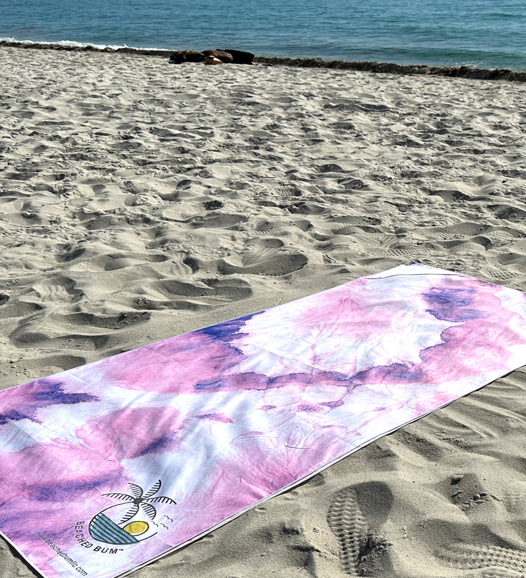 Pink and purple tie-dye towel on a sandy beach with ocean in the background